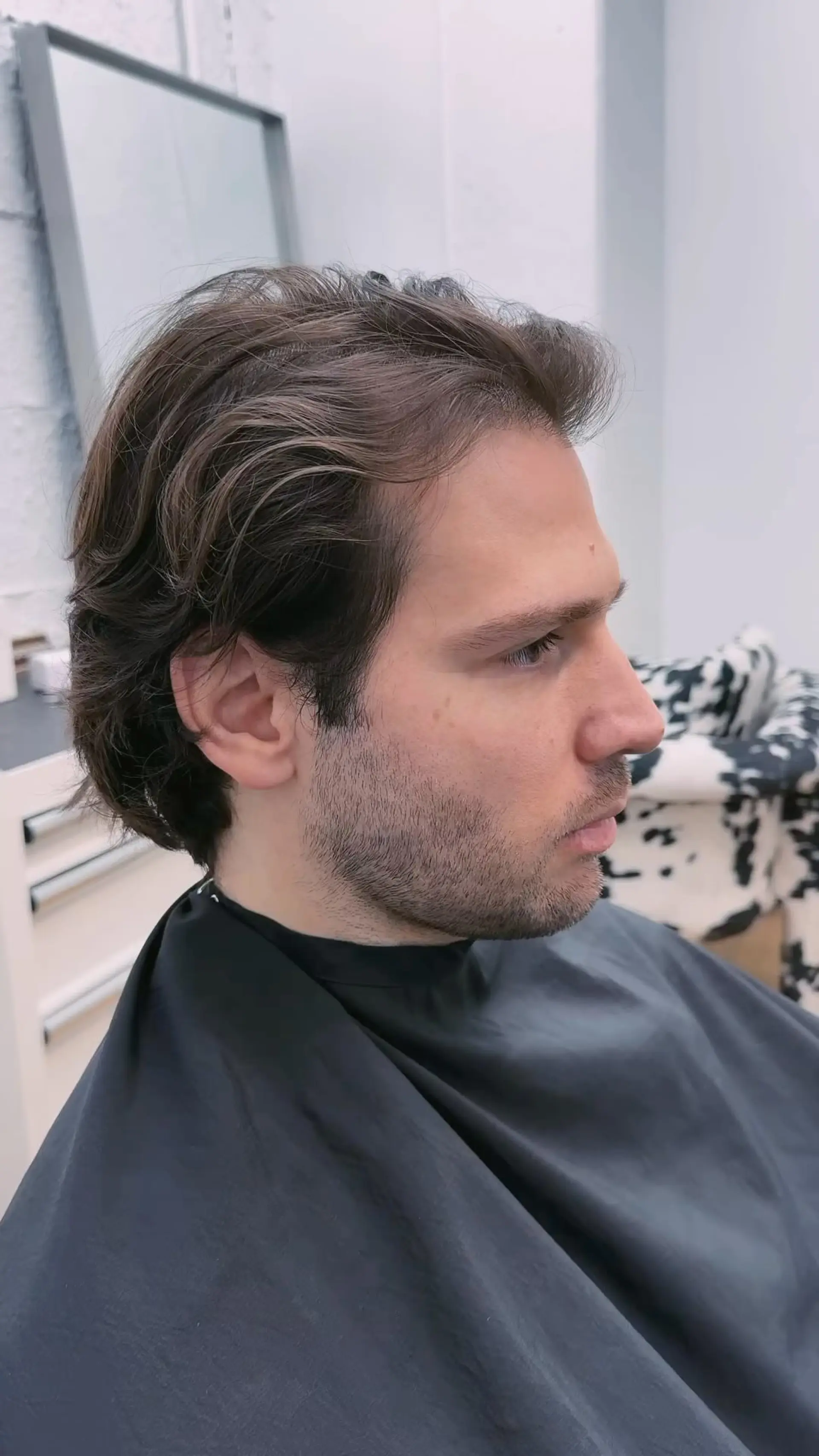 A men's medium-to-short layered cut styled pushed back naturally from the face with soft texture. 1