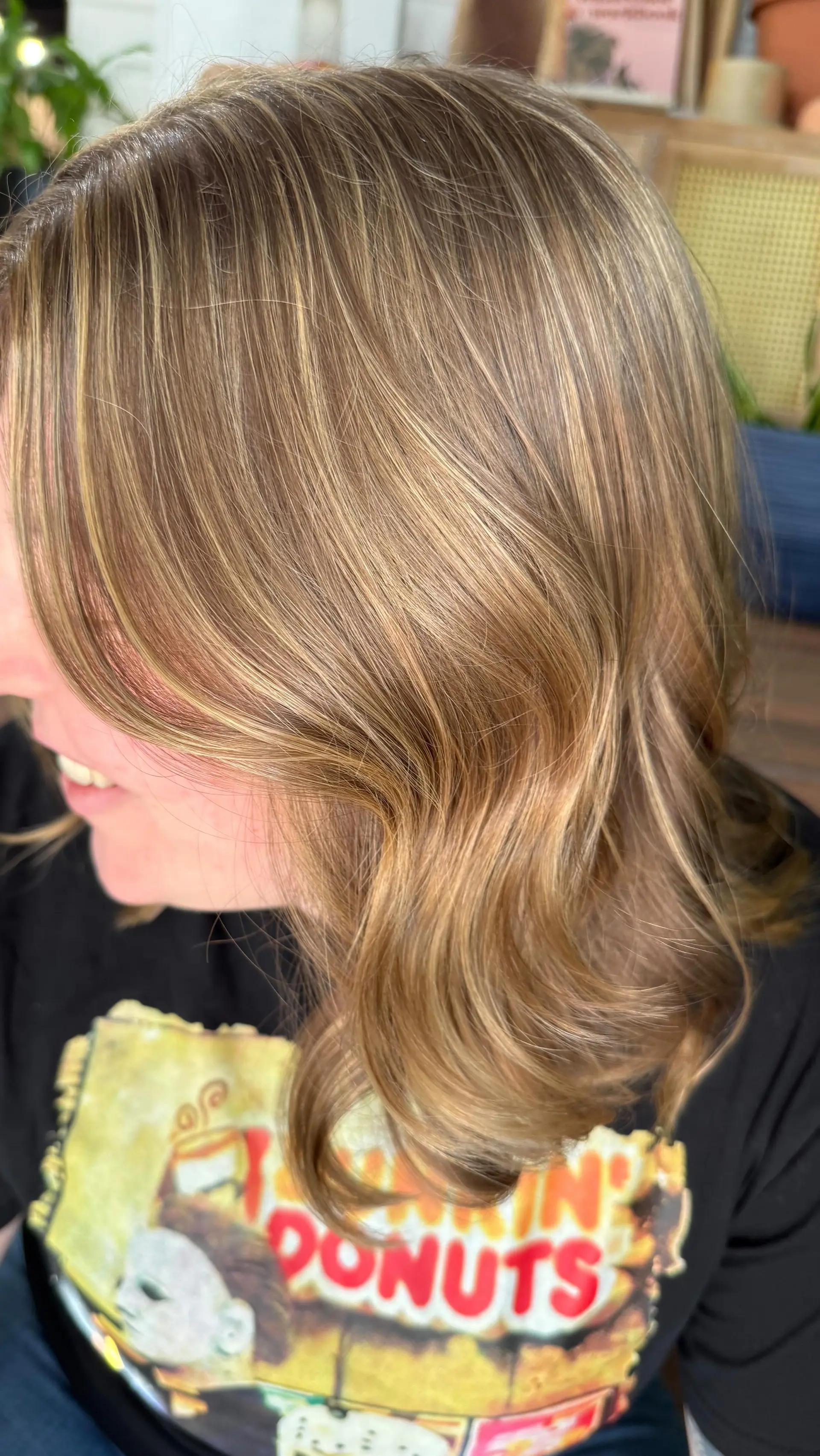 Medium-length light brown hair enhanced with fine honey blonde highlights and styled into smooth, bouncy waves. 1