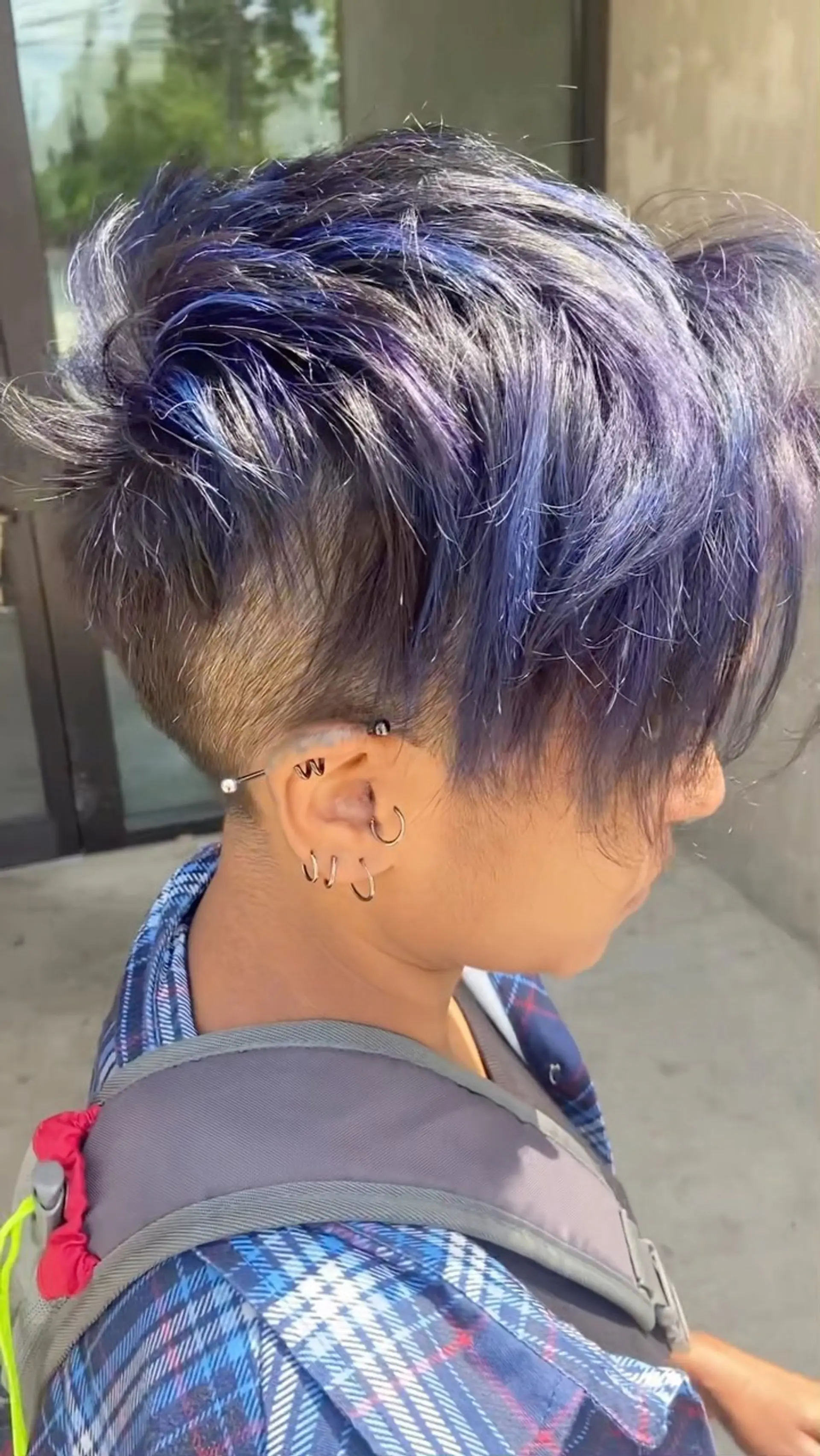 A textured short pixie cut featuring a shaved undercut on the side and piecey layers with blue and purple tones on top. 1