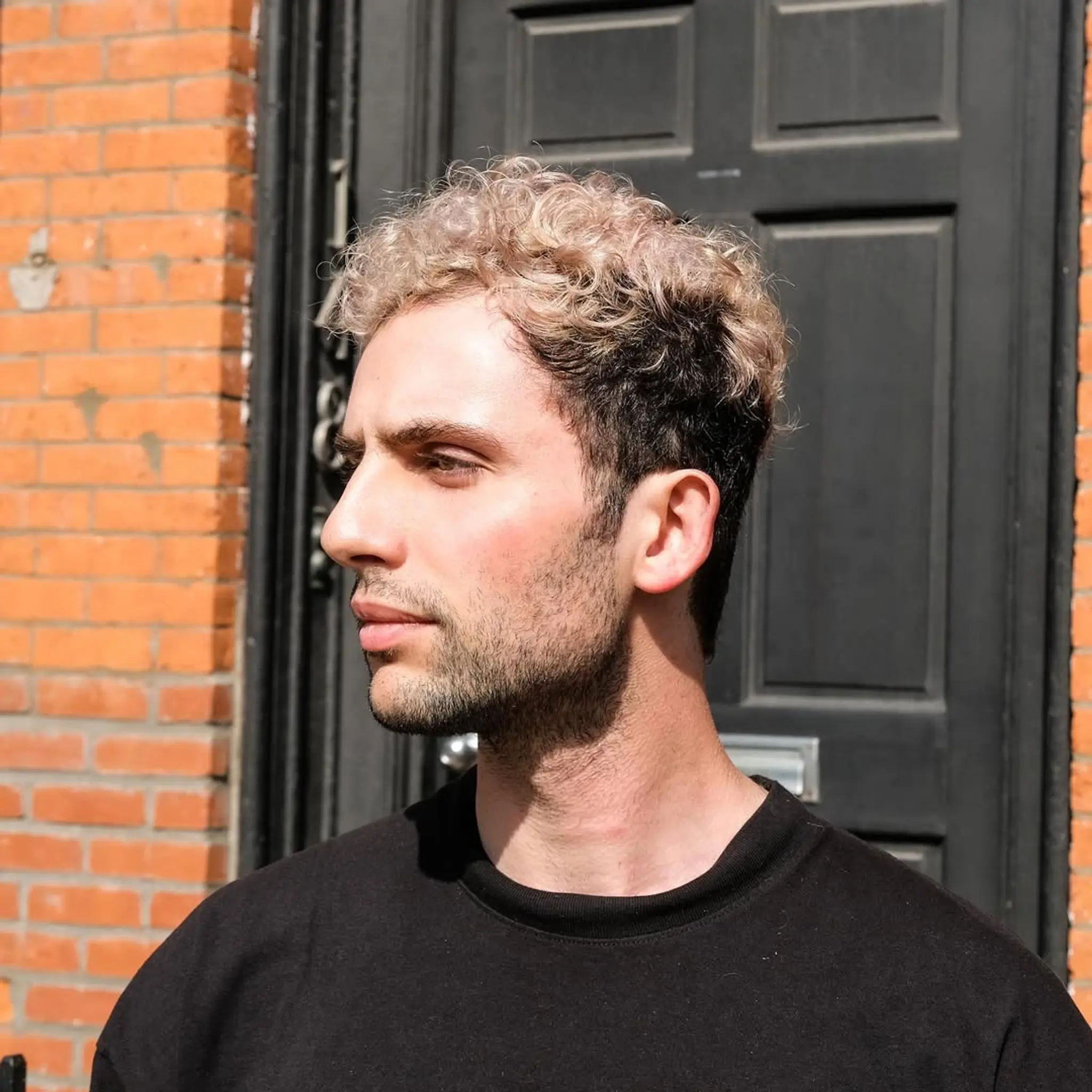 Short, curly hair with a stylish fade on the sides. Blonde and brown gradient on top.