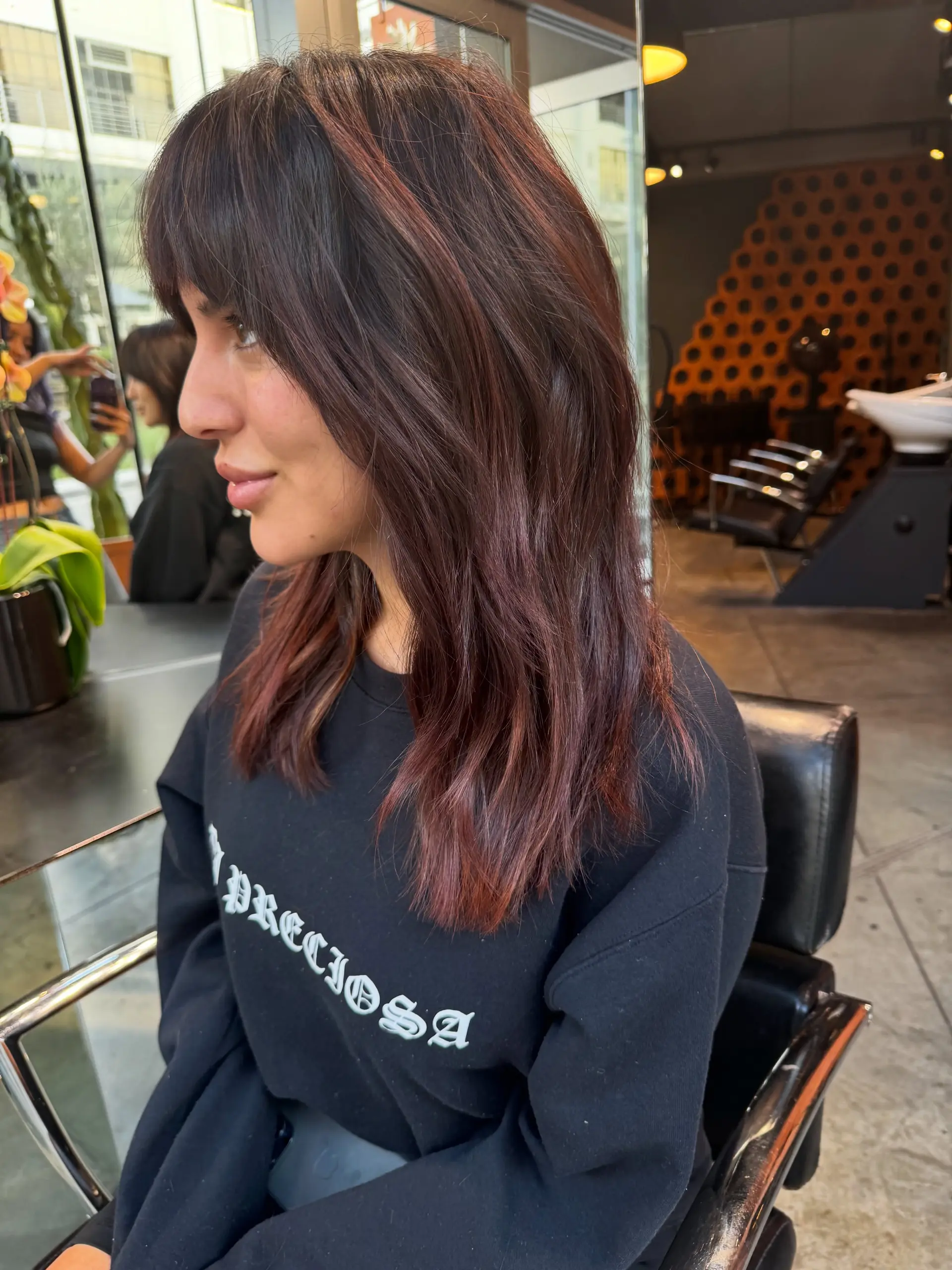A medium-length textured haircut with soft layers and full fringe, featuring warm auburn tones over dark brown hair. 1