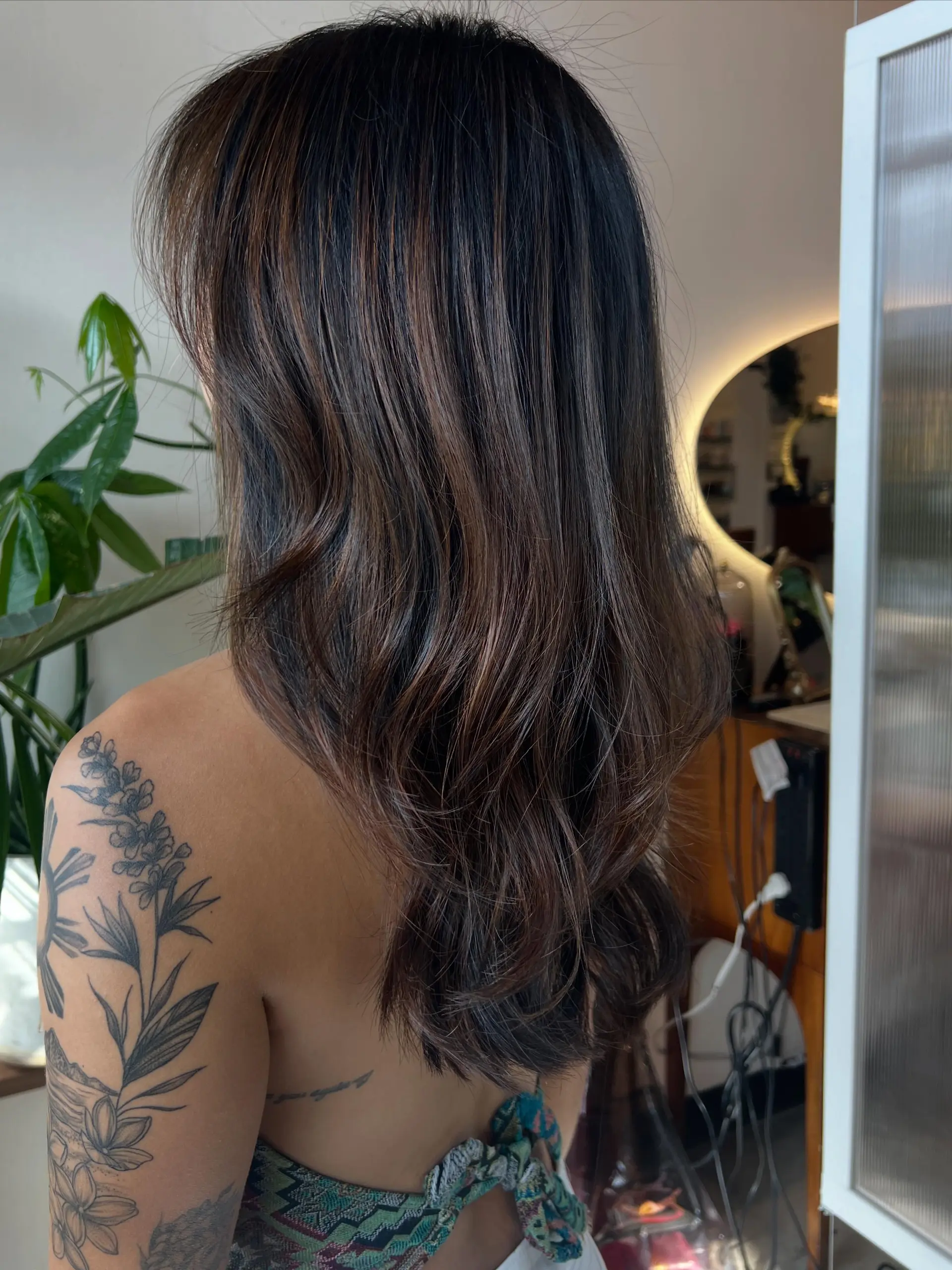 Long layered dark brunette hair detailed with fine, warm brown balayage highlights and styled into soft, flowing waves. 1