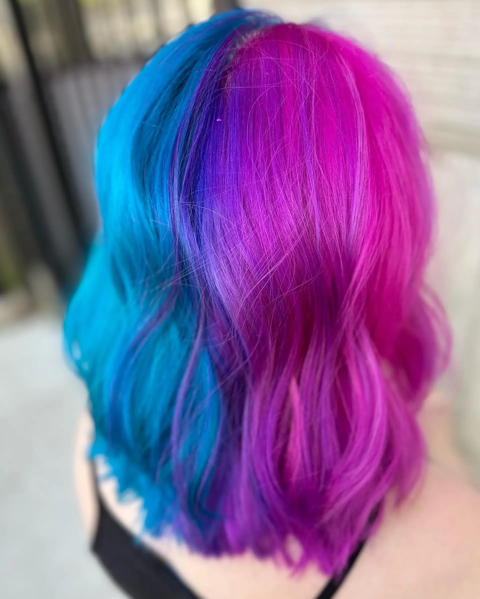 A bold split-dye style featuring electric cyan blue on one half and vivid magenta blending into purple on the other, styled in soft waves. 1