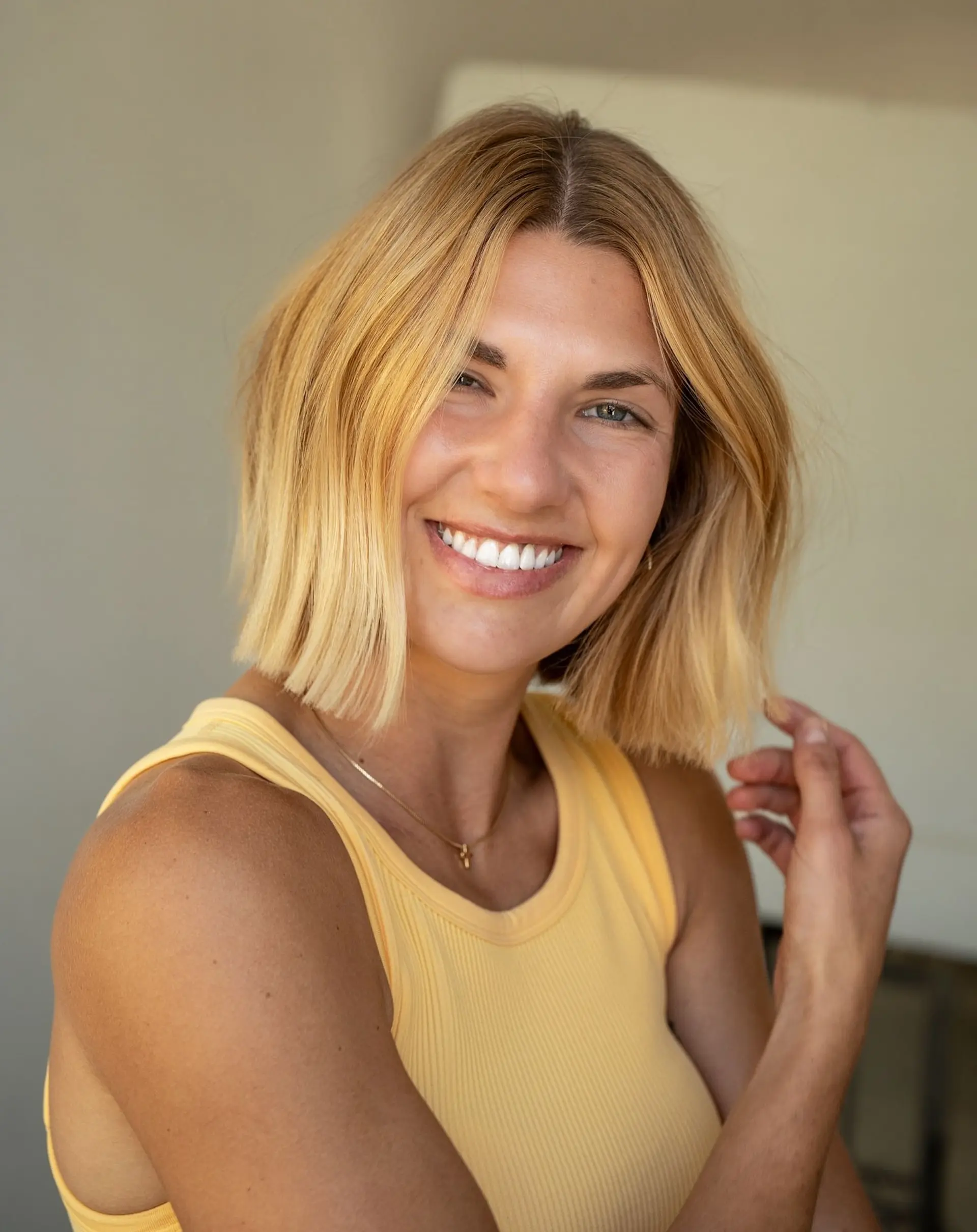 A textured blunt bob cut falling just below the chin, styled straight with soft movement in a radiant warm golden blonde. 1