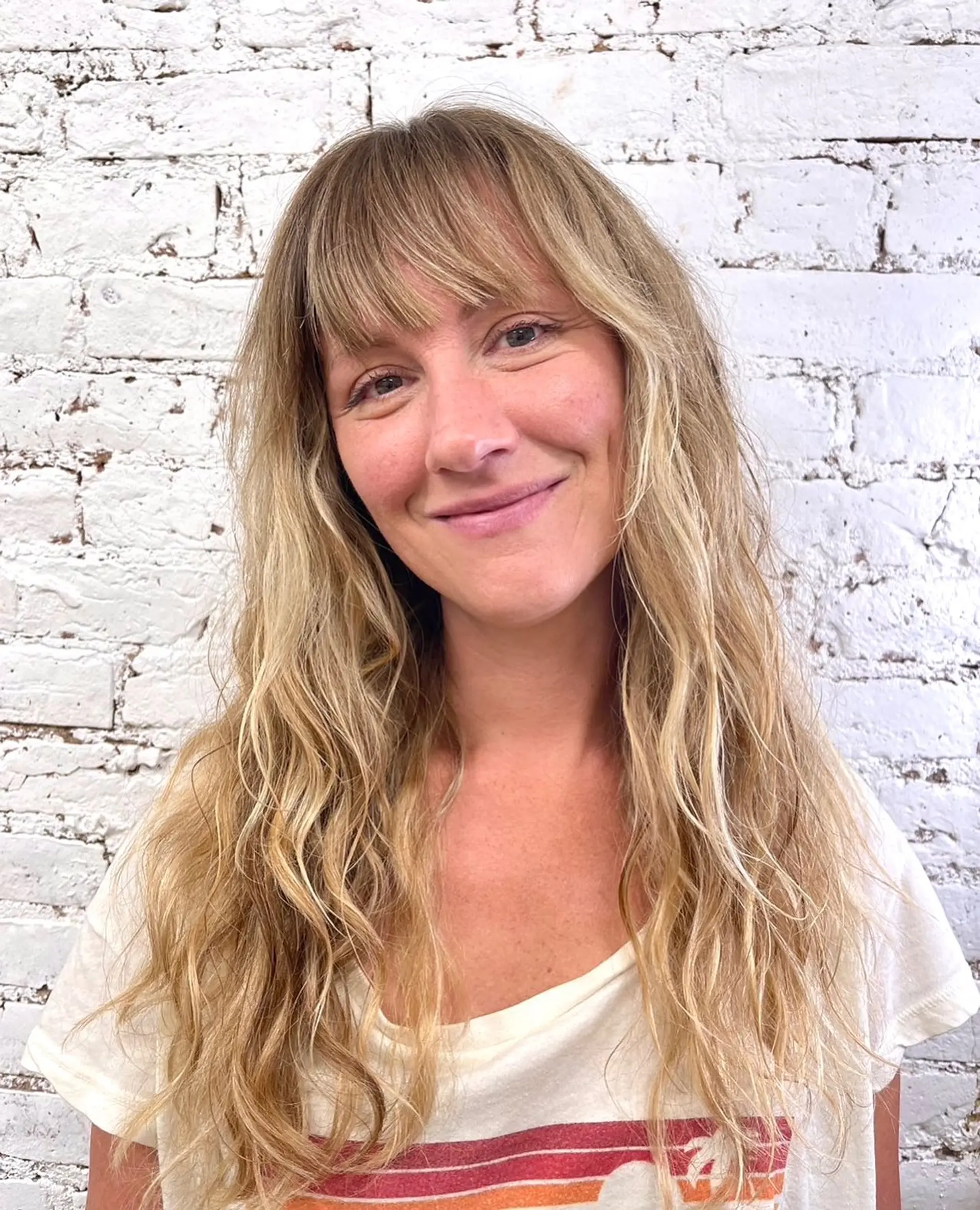 Long sun-kissed blonde hair styled with tousled, beachy waves and a full fringe. 1