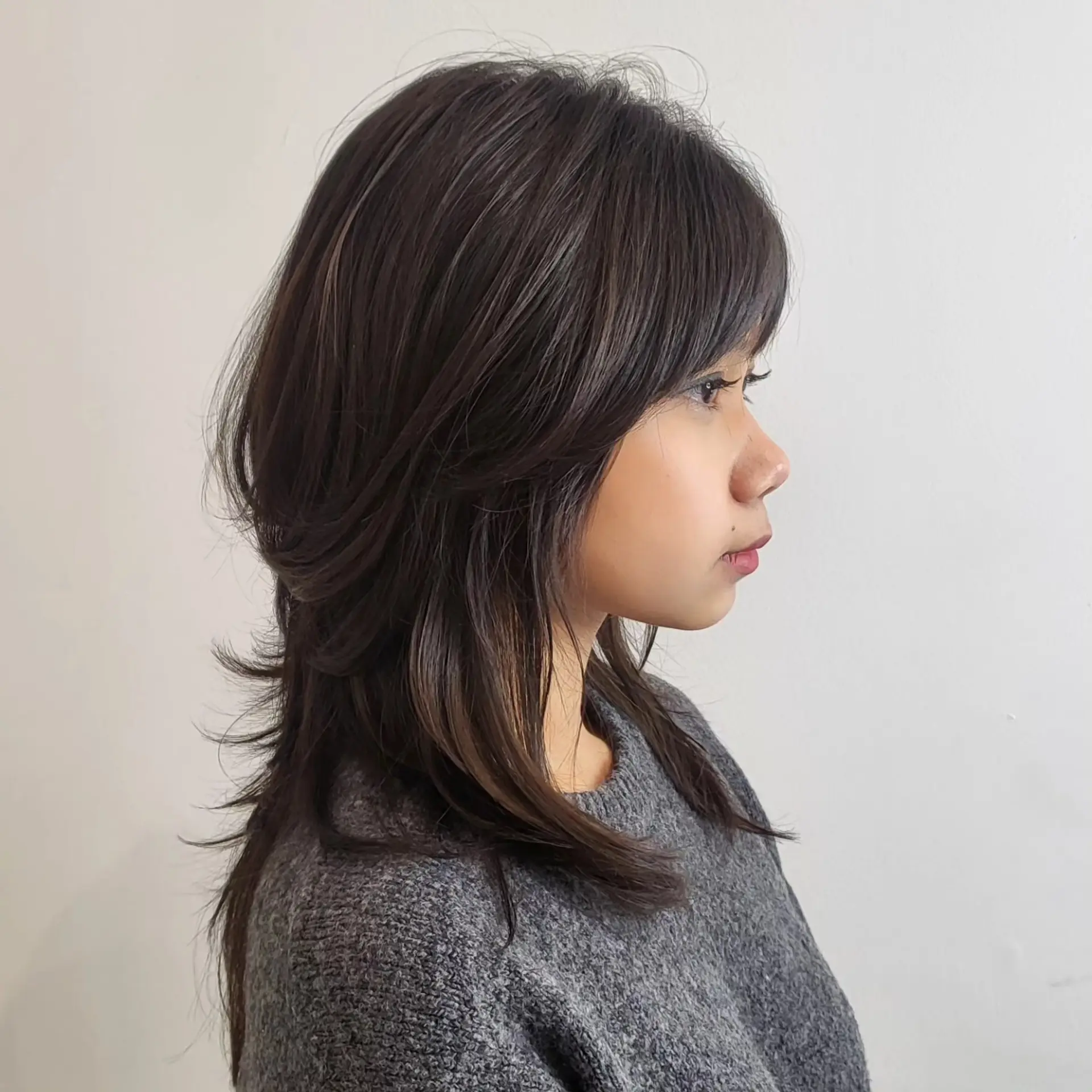 Medium-length layered haircut with soft feathered ends and full brow-skimming bangs. 1