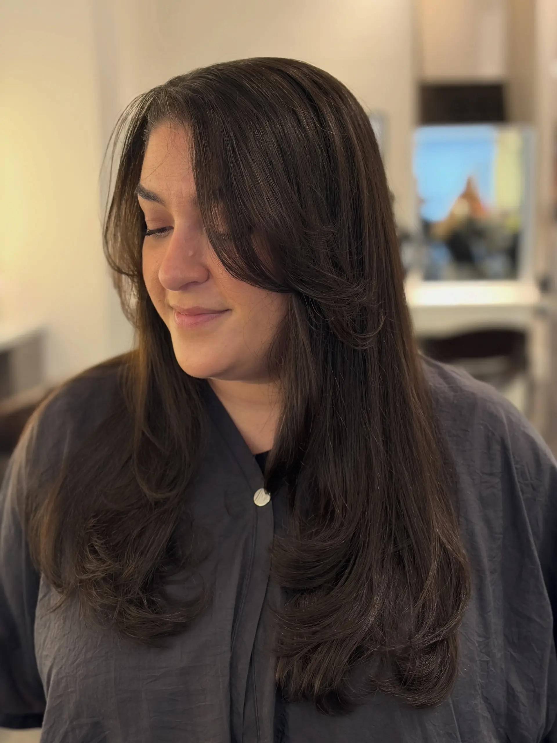 Long dark brunette hair featuring face-framing layers and long bangs, styled in a sleek, bouncy blowout with curved ends. 1