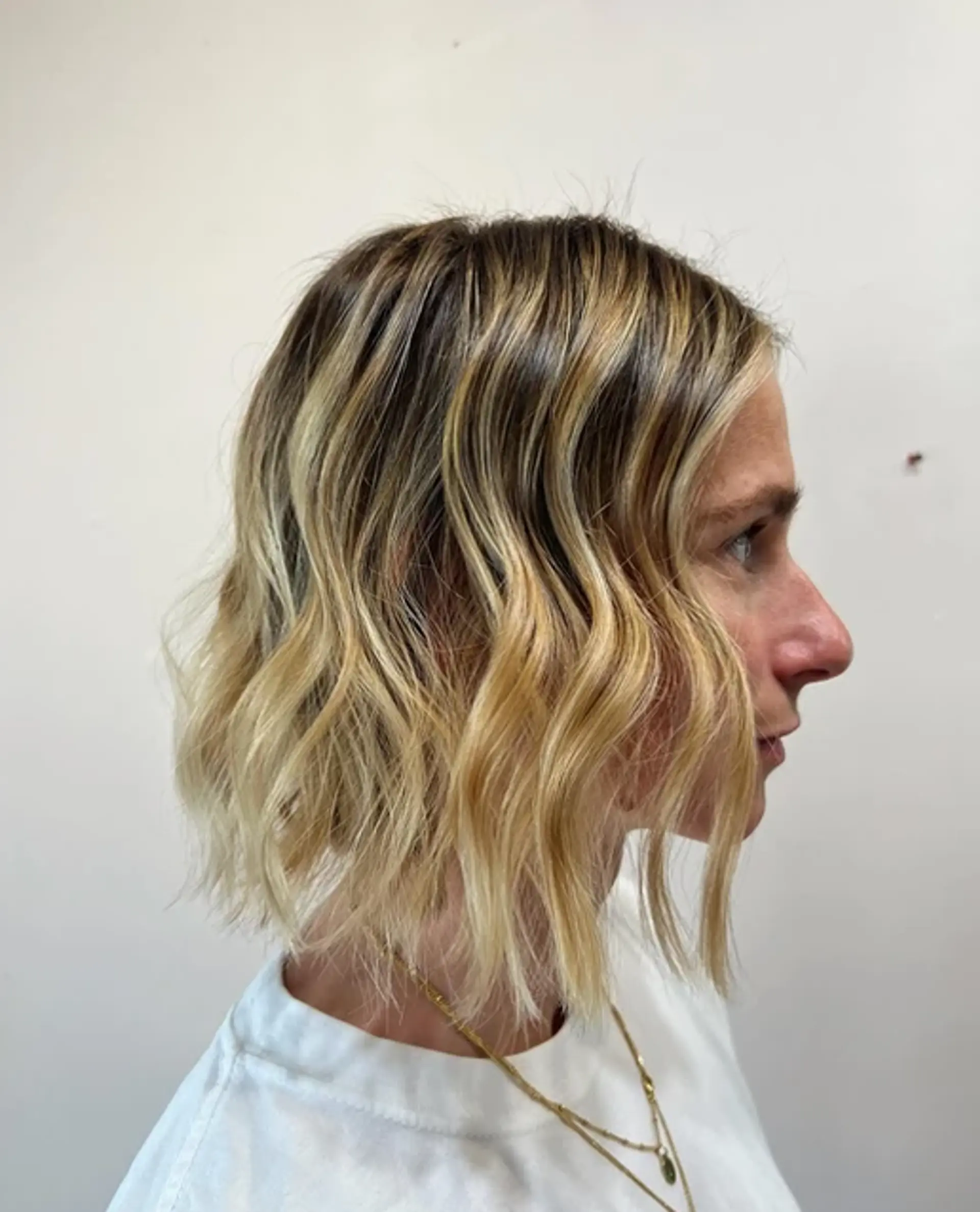 A short, wavy bob with a sun-kissed blonde hue and natural dark roots. 1