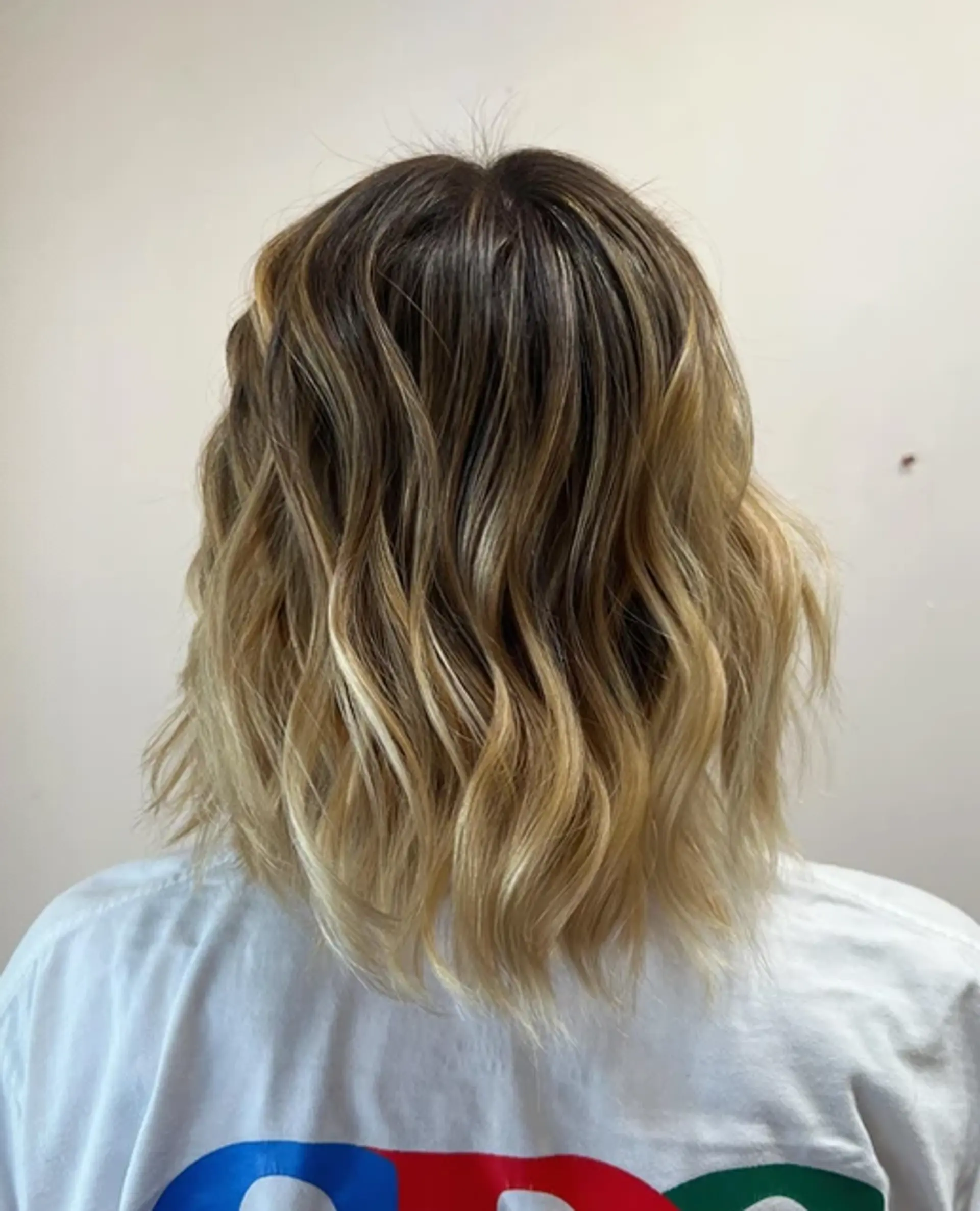 A short, wavy bob with a sun-kissed blonde hue and natural dark roots. 2