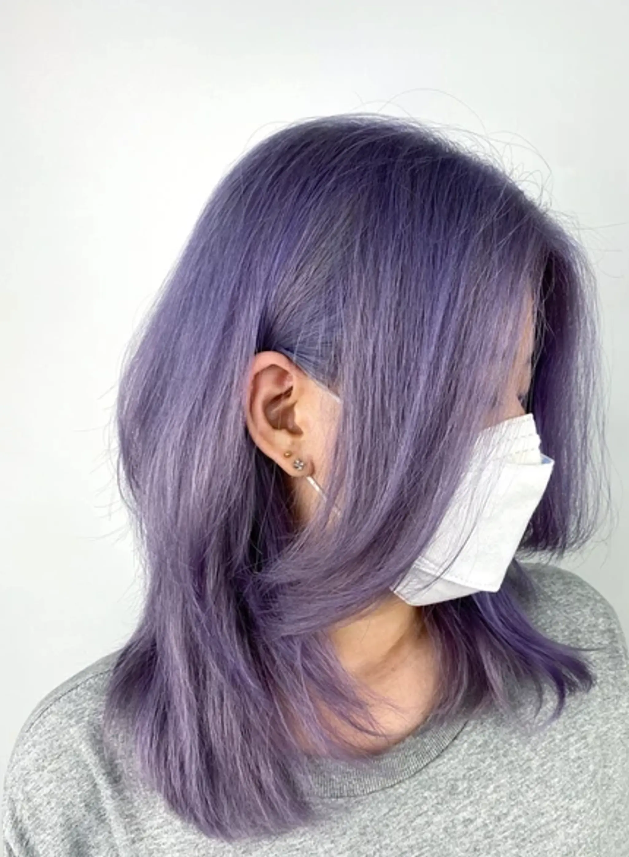 Medium-length, straight hair with a vibrant lavender and light purple color. Layered with full bangs, showcasing ashy tones.