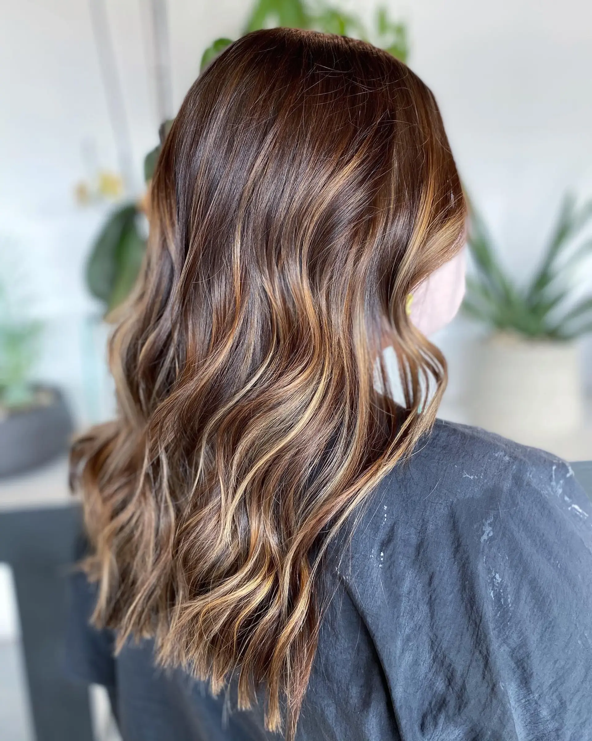 Rich brunette hair painted with warm caramel balayage highlights and styled into soft, dimensional waves. 1