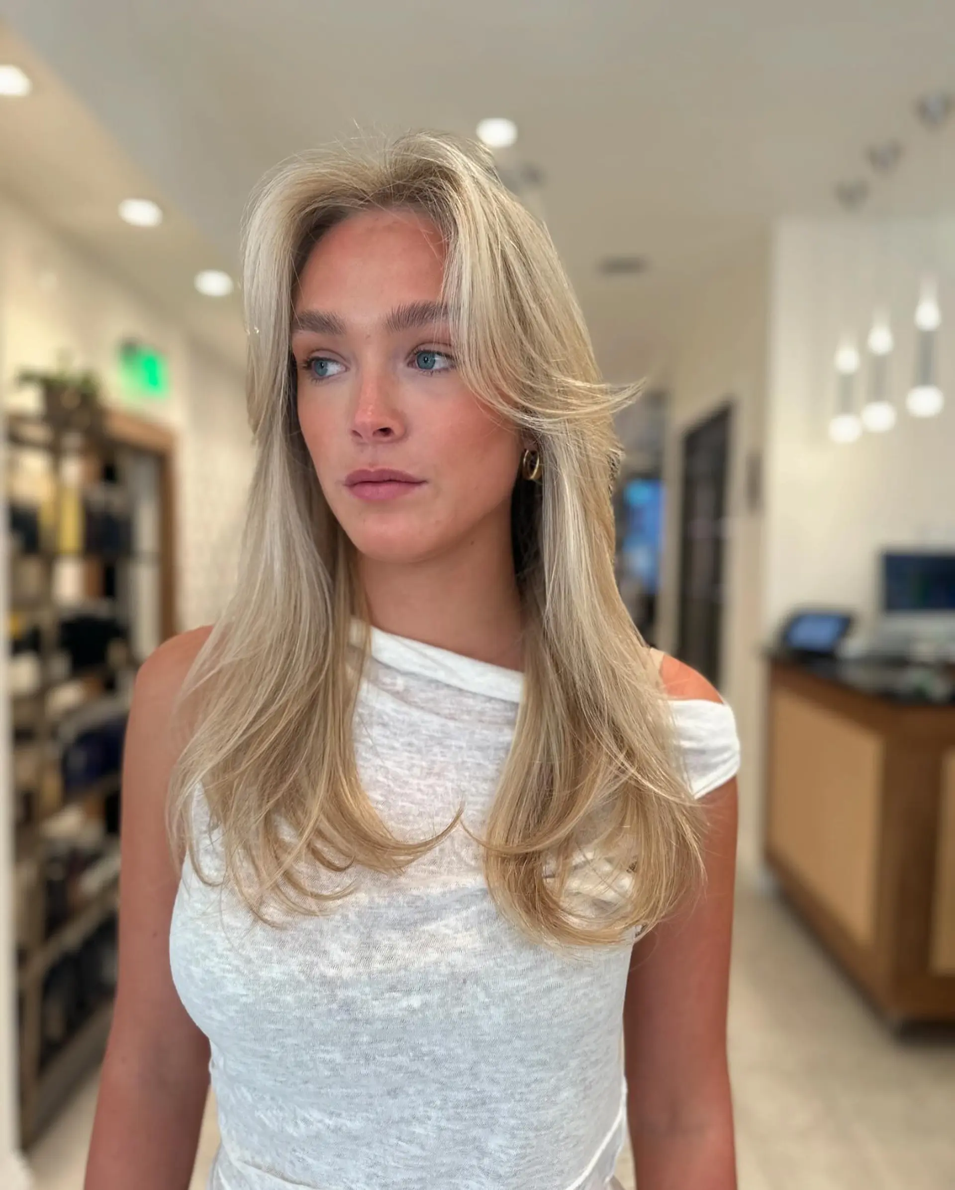 Long creamy blonde hair cut with curtain bangs and styled in a bouncy blowout. 1