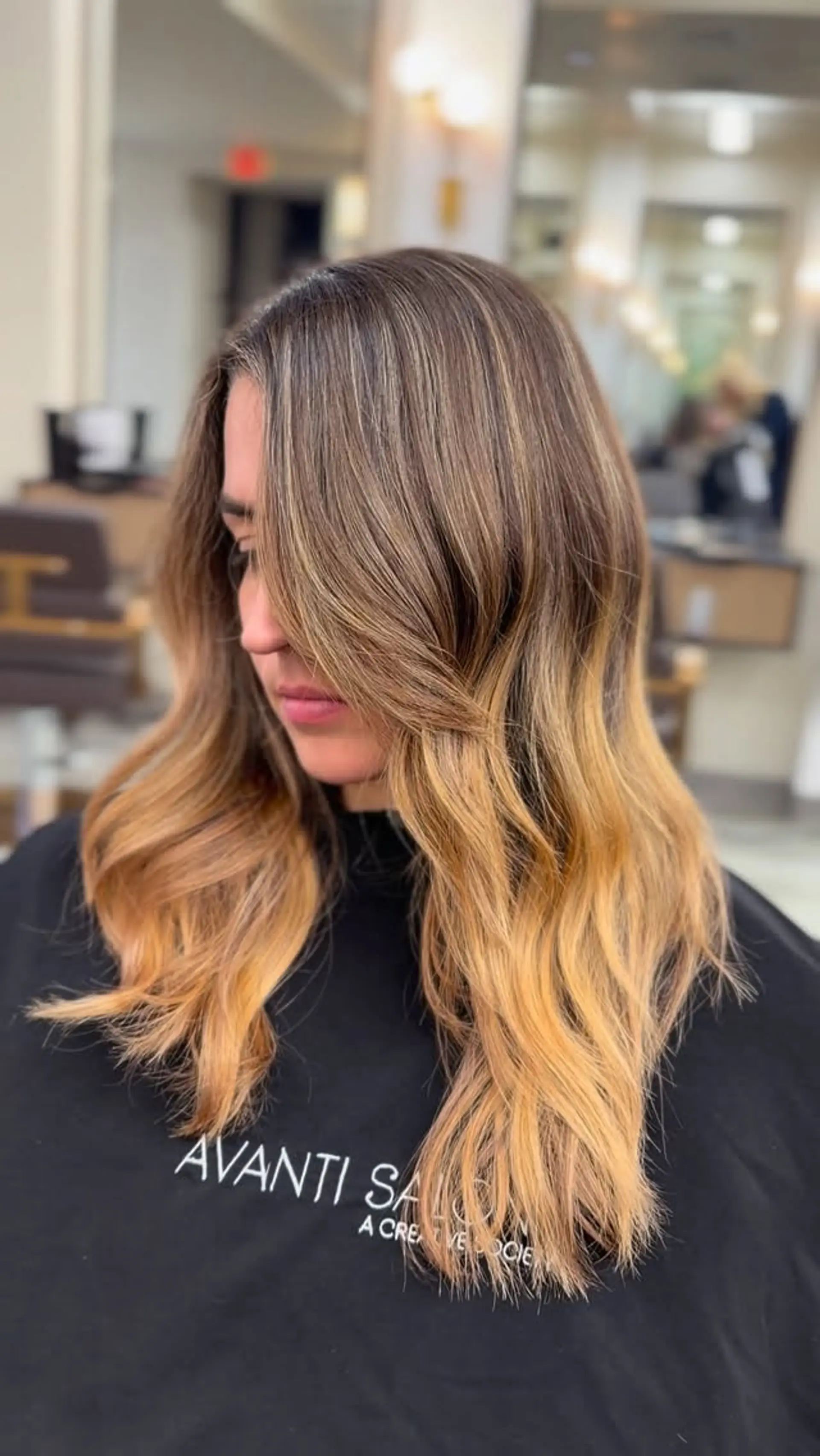 Long brown hair with a warm caramel balayage ombre styled into smooth, loose blowout waves. 1