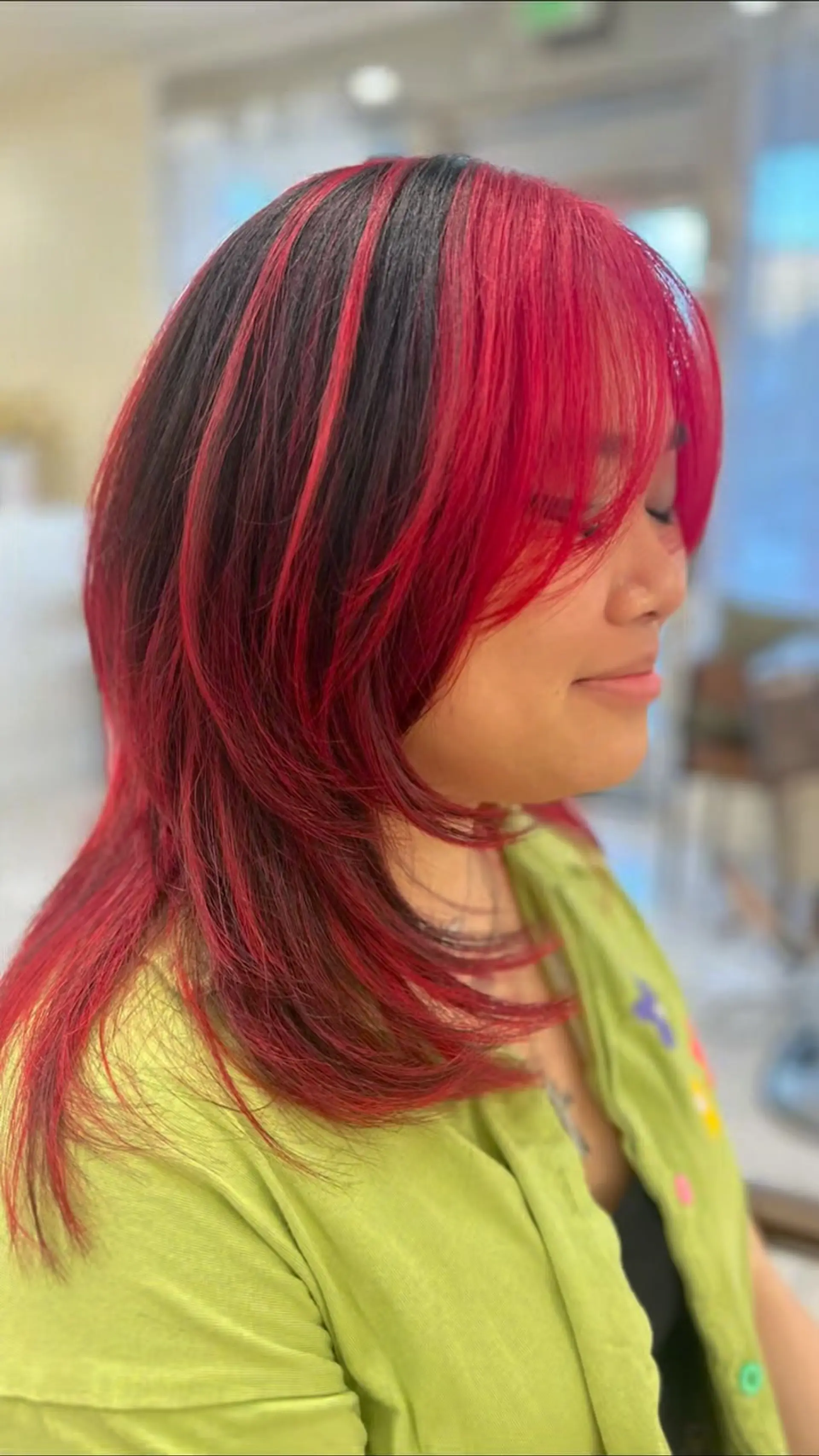 A medium-length layered hush cut styled with face-framing layers, soft wispy bangs, and vibrant cherry red color blocking over a black base. 1