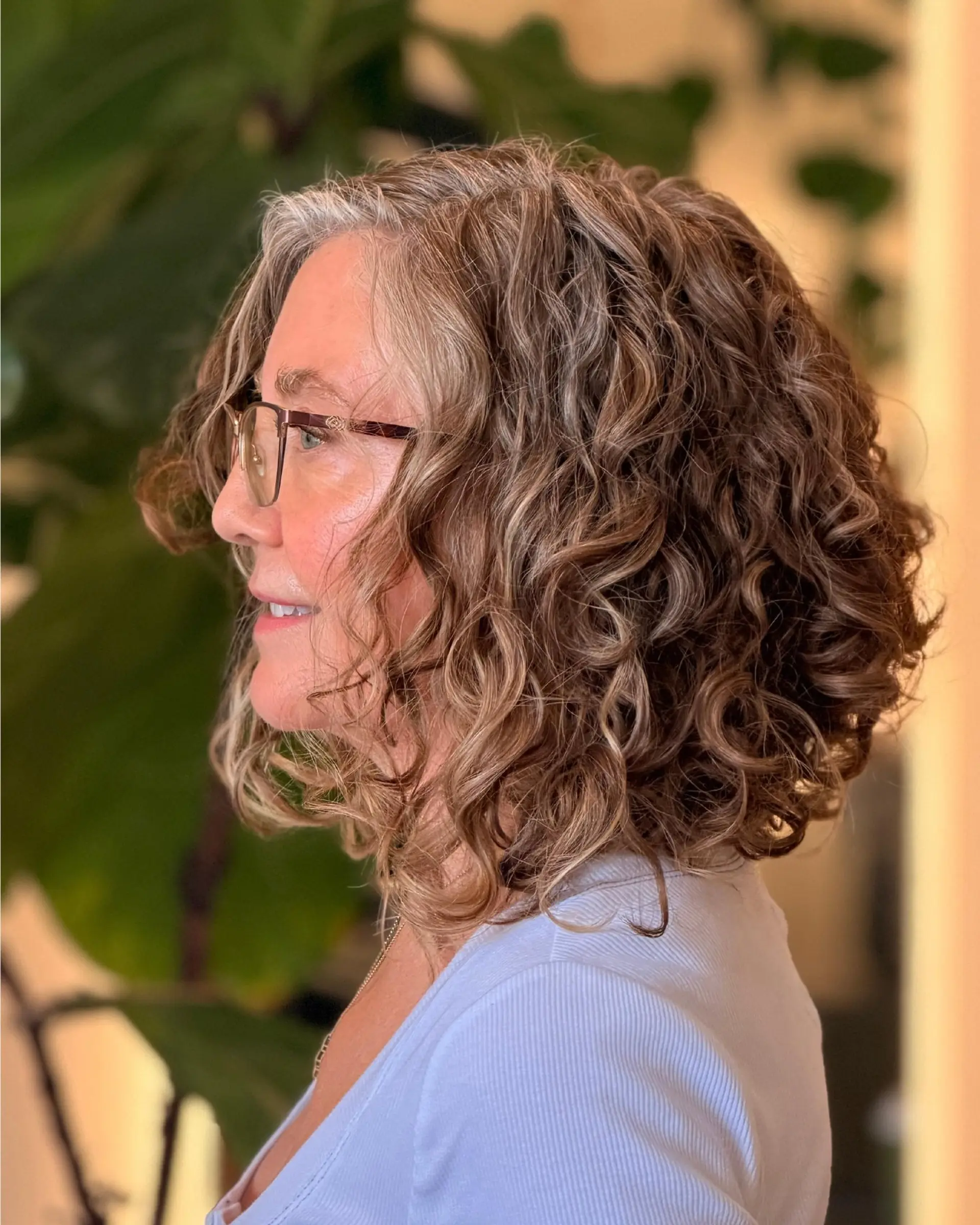 A textured shoulder-length curly cut with bouncy, defined ringlets and warm dimensional highlights blended into natural gray. 1