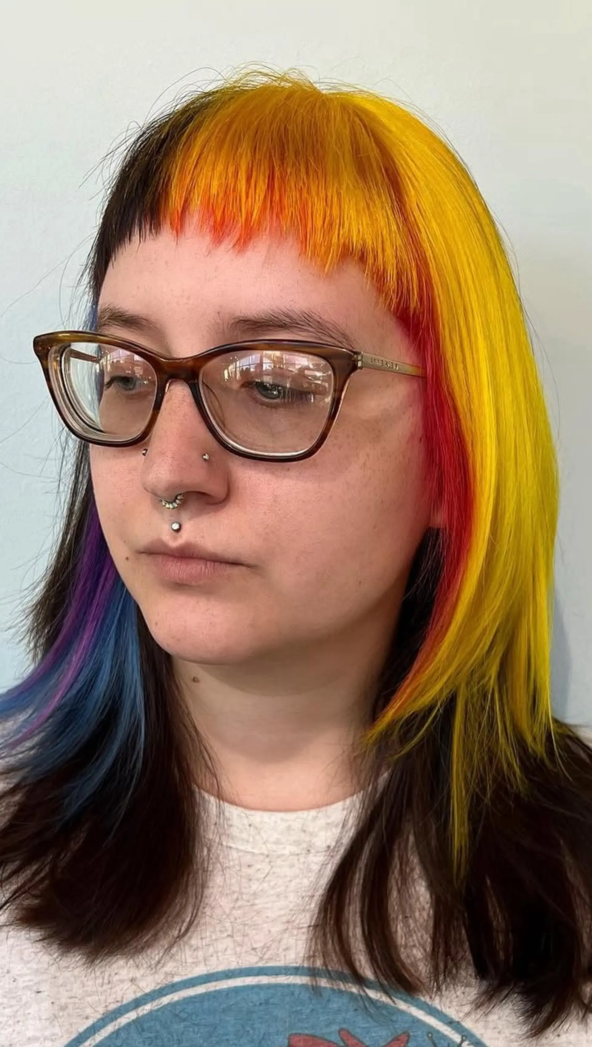 A striking color-blocked look featuring chopped micro bangs and straight shoulder-length hair with vivid yellow, orange, red, and peekaboo blue-violet tones. 1
