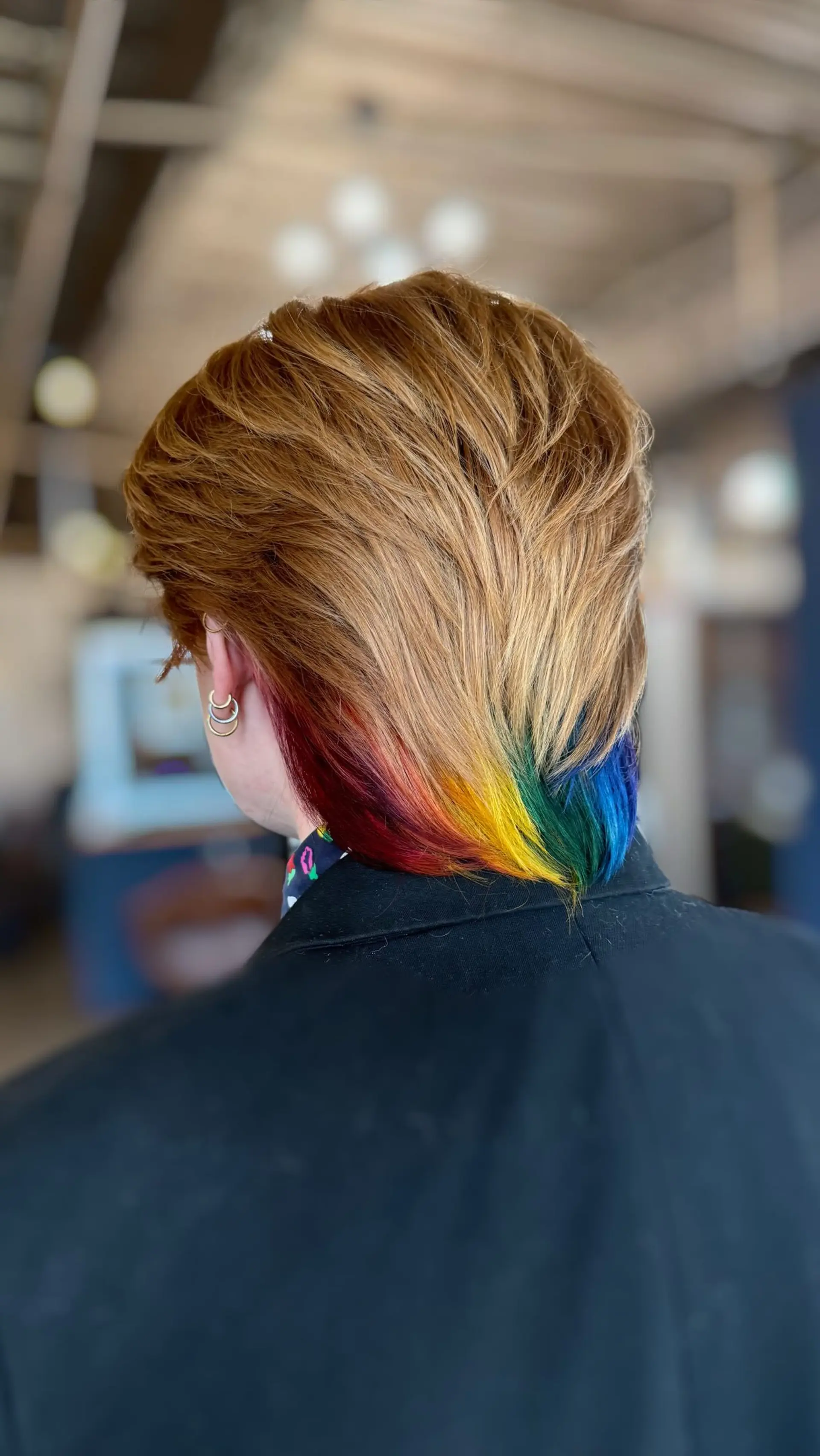 A feathered, swept-back short cut with warm golden-blonde layers over a vibrant rainbow peekaboo panel at the nape. 1