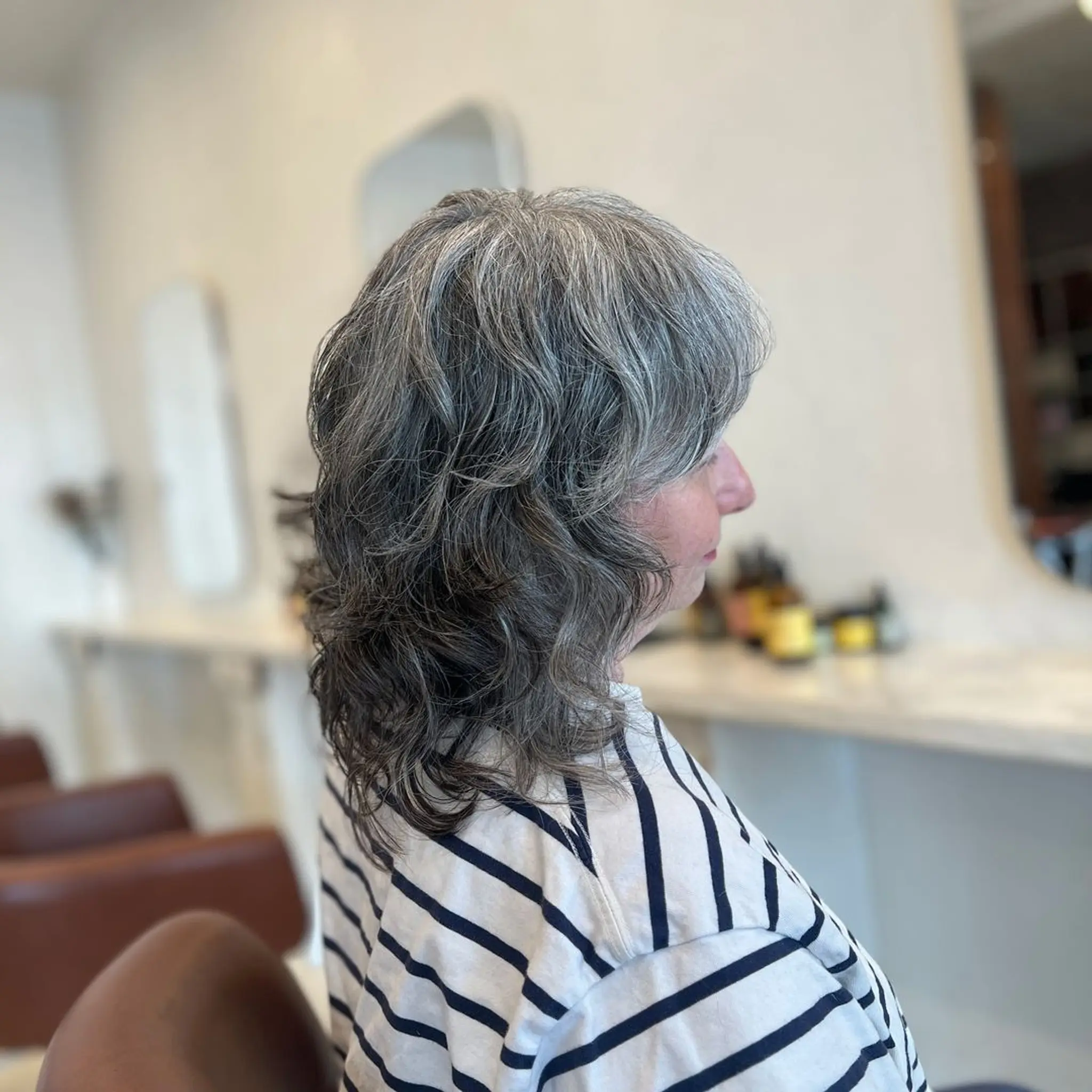 A medium-length, wavy hairstyle with a natural blend of grey and black hair, featuring soft layers and a side part.