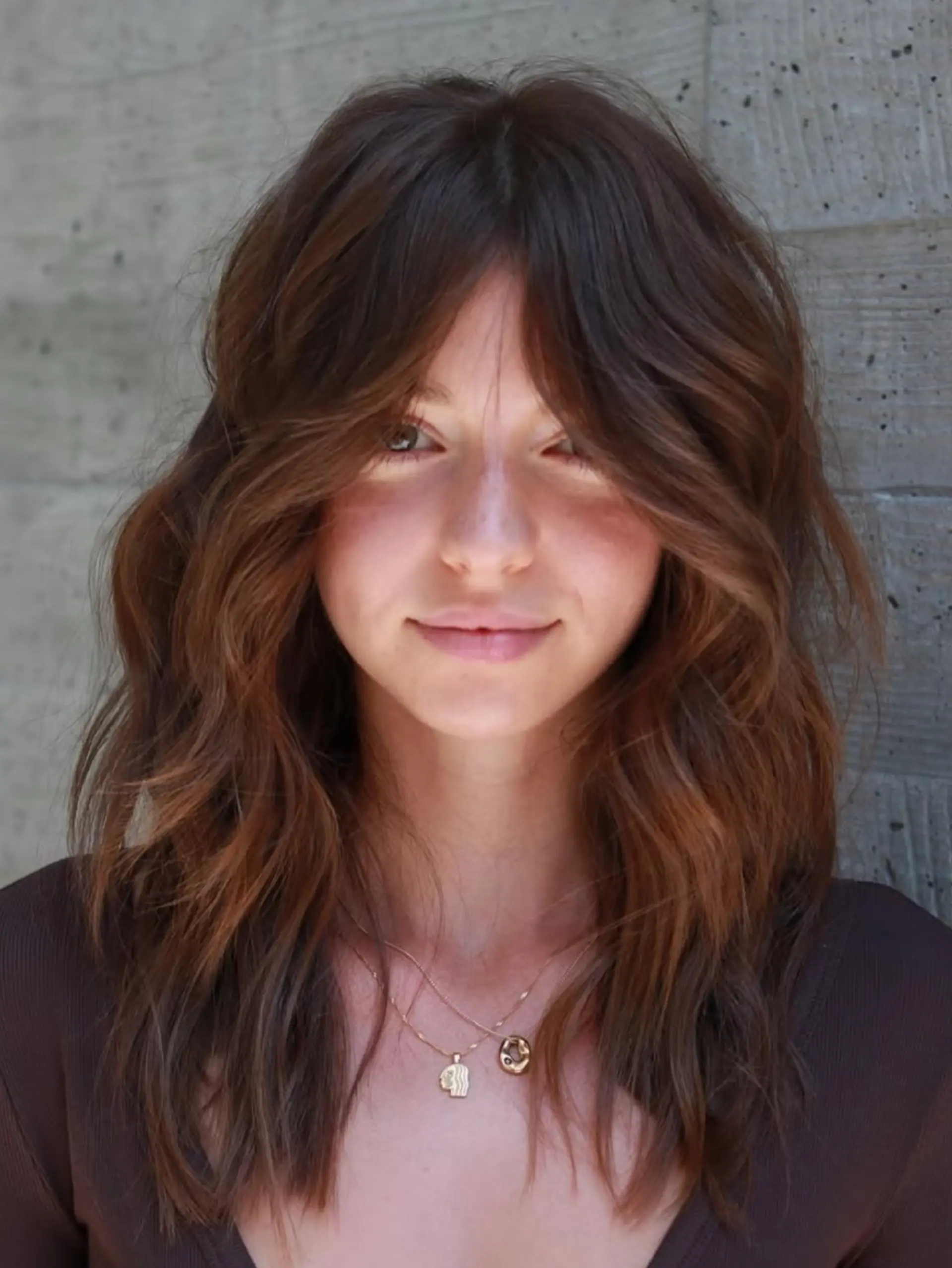 Medium-length layered haircut featuring voluminous curtain bangs and soft, textured waves. 1