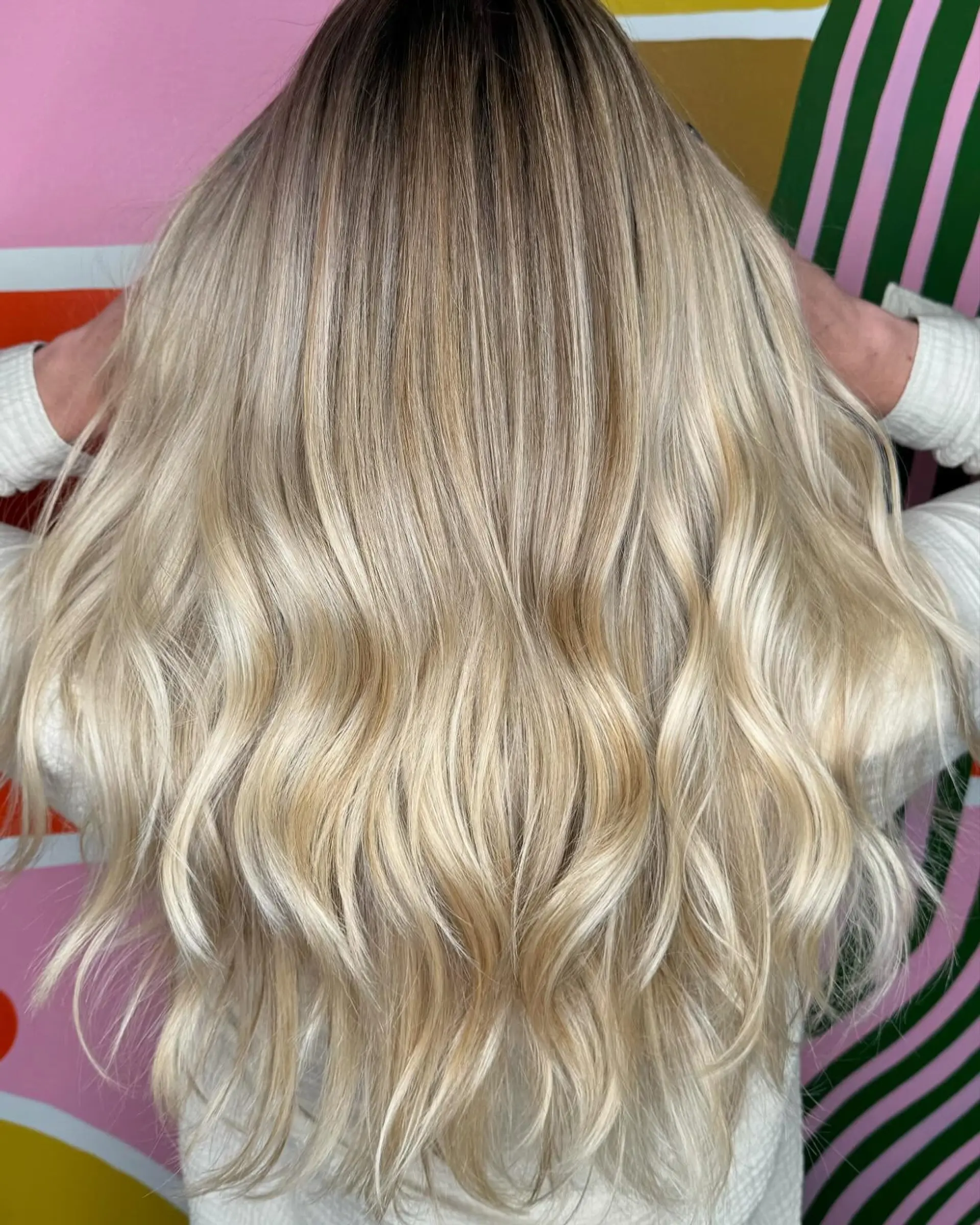 A long, dimensional platinum blonde style featuring a soft shadow root that seamlessly blends into bright, luminous blonde lengths styled with loose, relaxed waves. 1