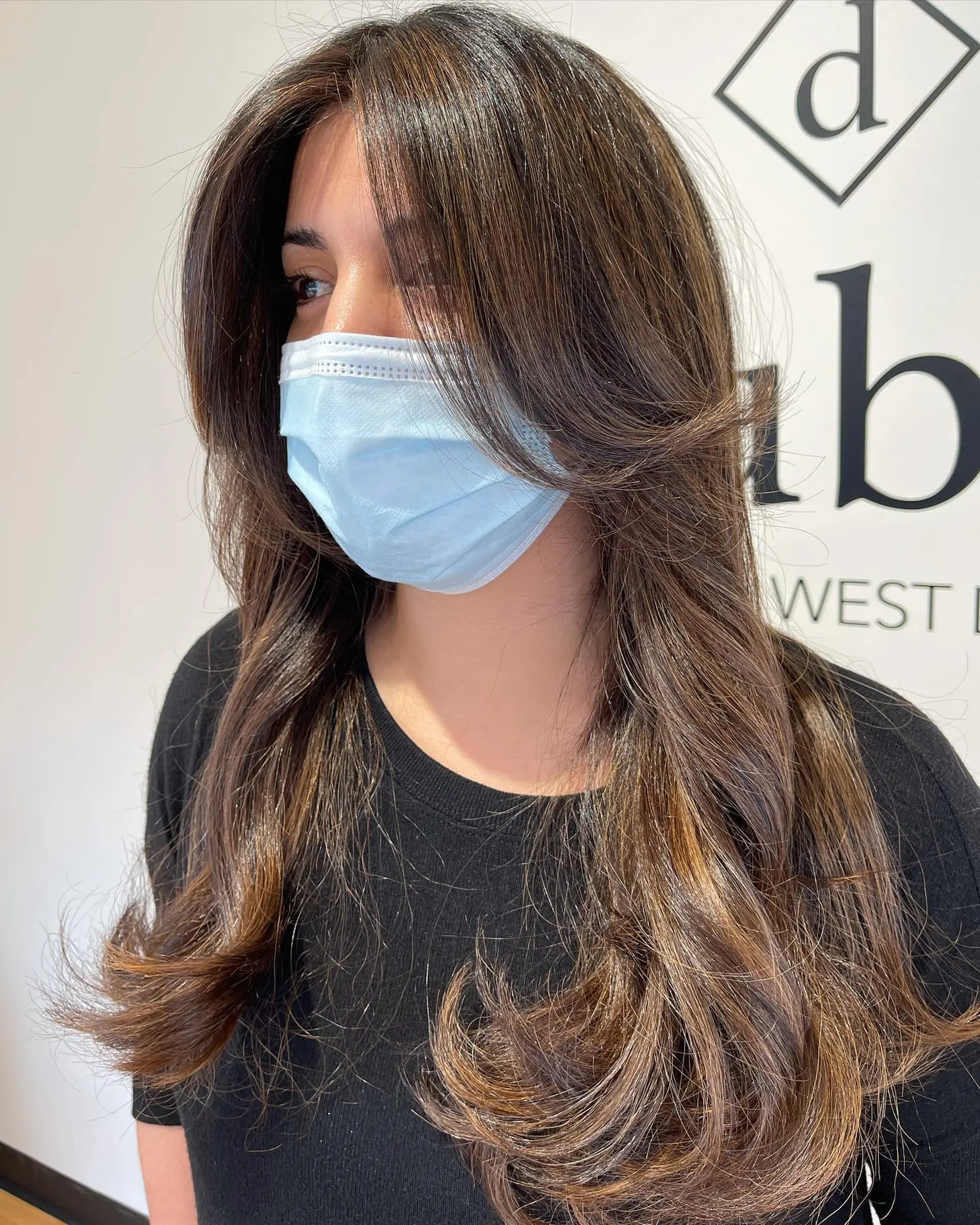Long dark brown hair styled with warm caramel highlights, layered face-framing curtain bangs, and soft flicked-out ends. 1