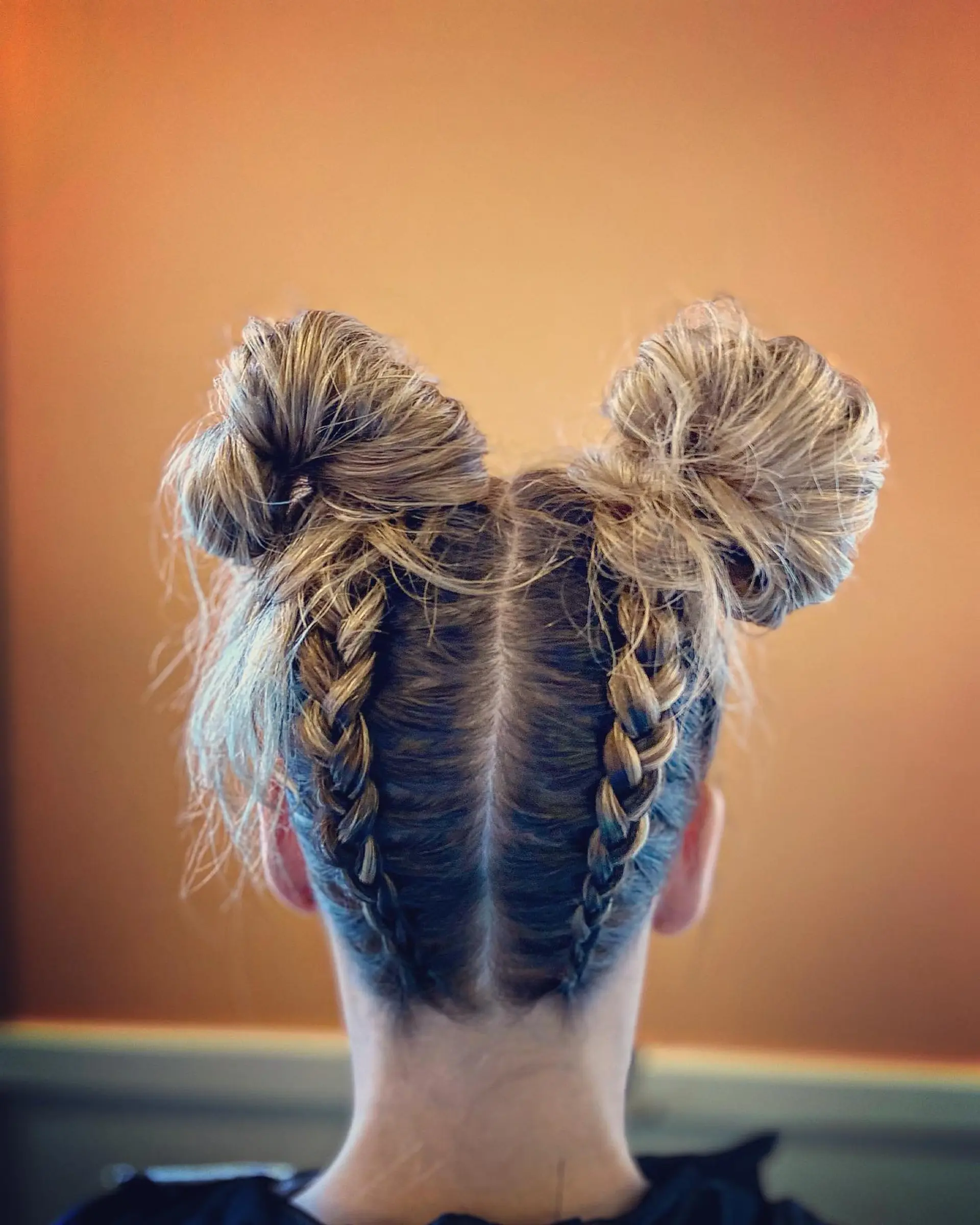 A playful updo featuring two reverse Dutch braids starting from the nape of the neck and finishing into voluminous, textured high space buns. 1