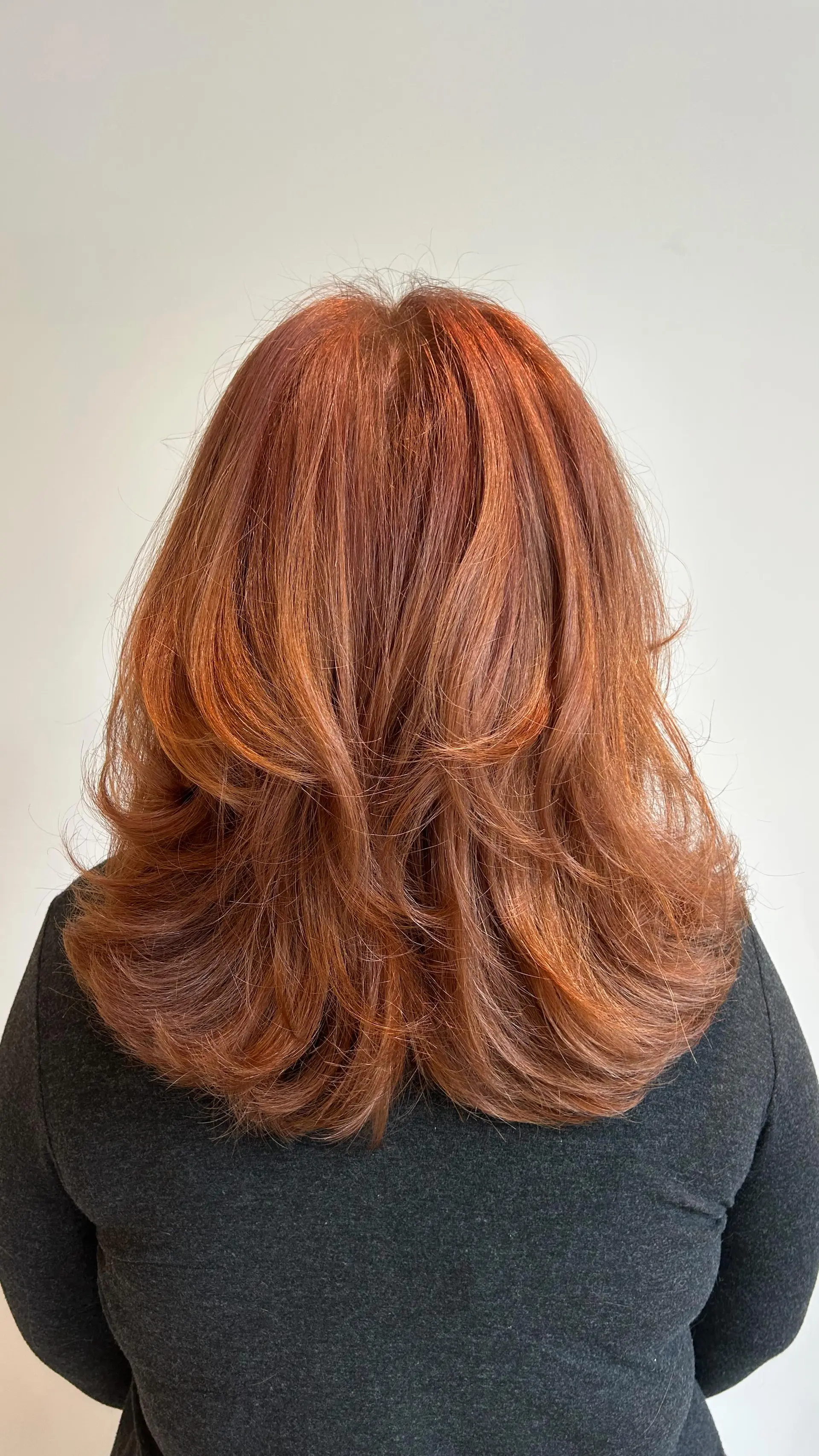 A voluminous, bouncy blowout on medium-length layered auburn hair with soft curled ends. 1