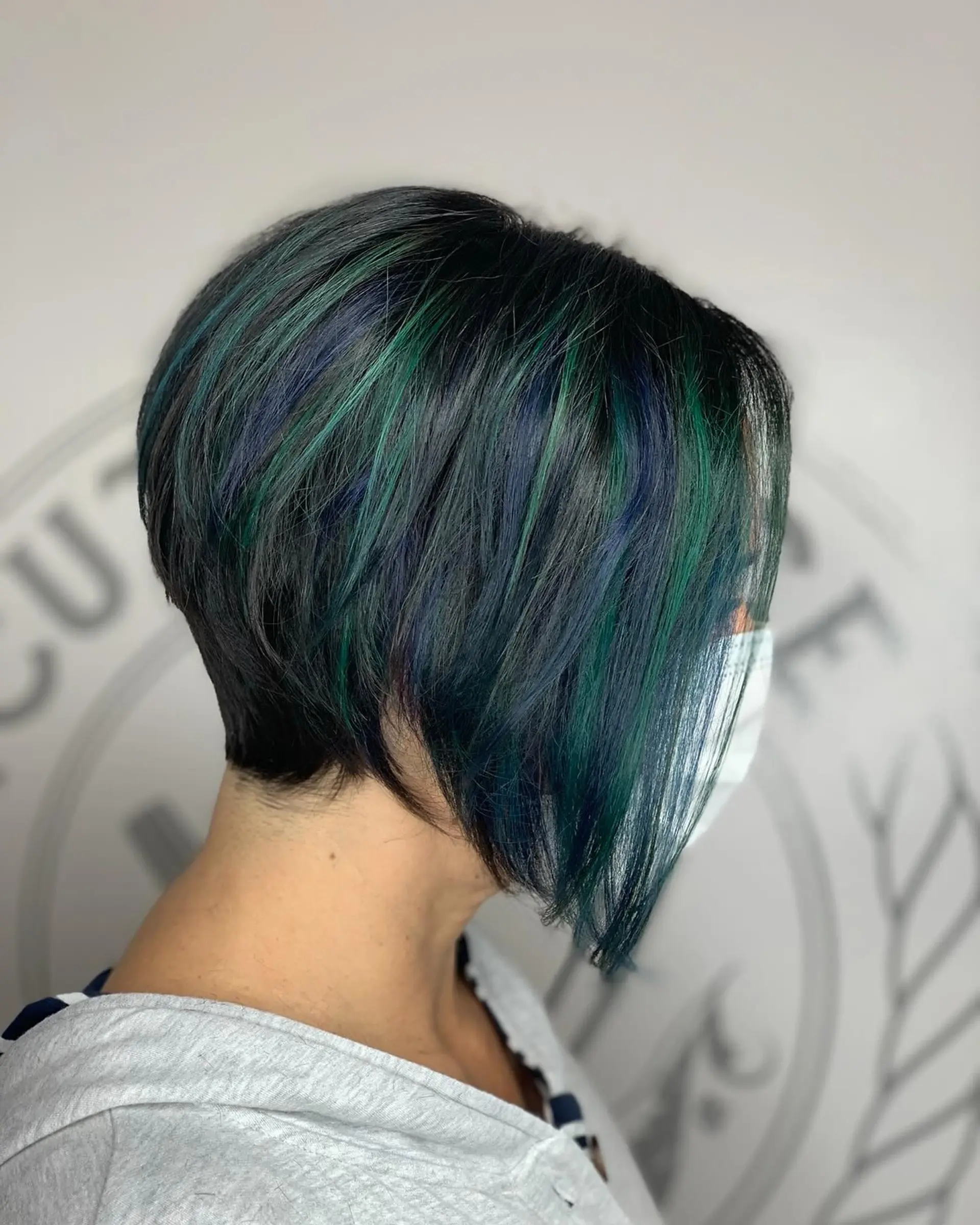 A textured, angled bob haircut featuring a dark base accented with dimensional emerald green and deep blue highlights. 1