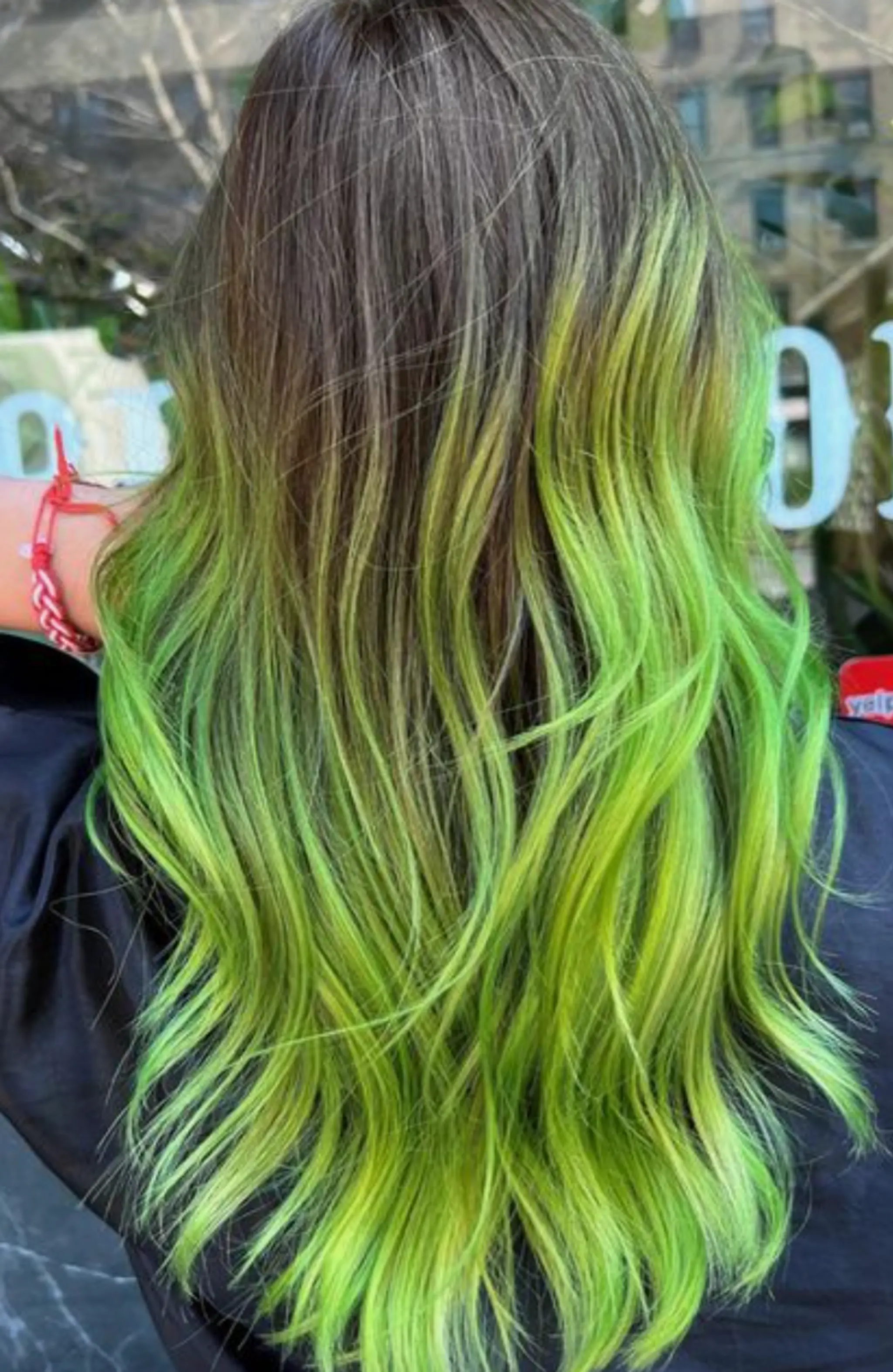 Long, wavy hair with natural brown roots that transition into vibrant neon green tips, creating a striking ombre effect.