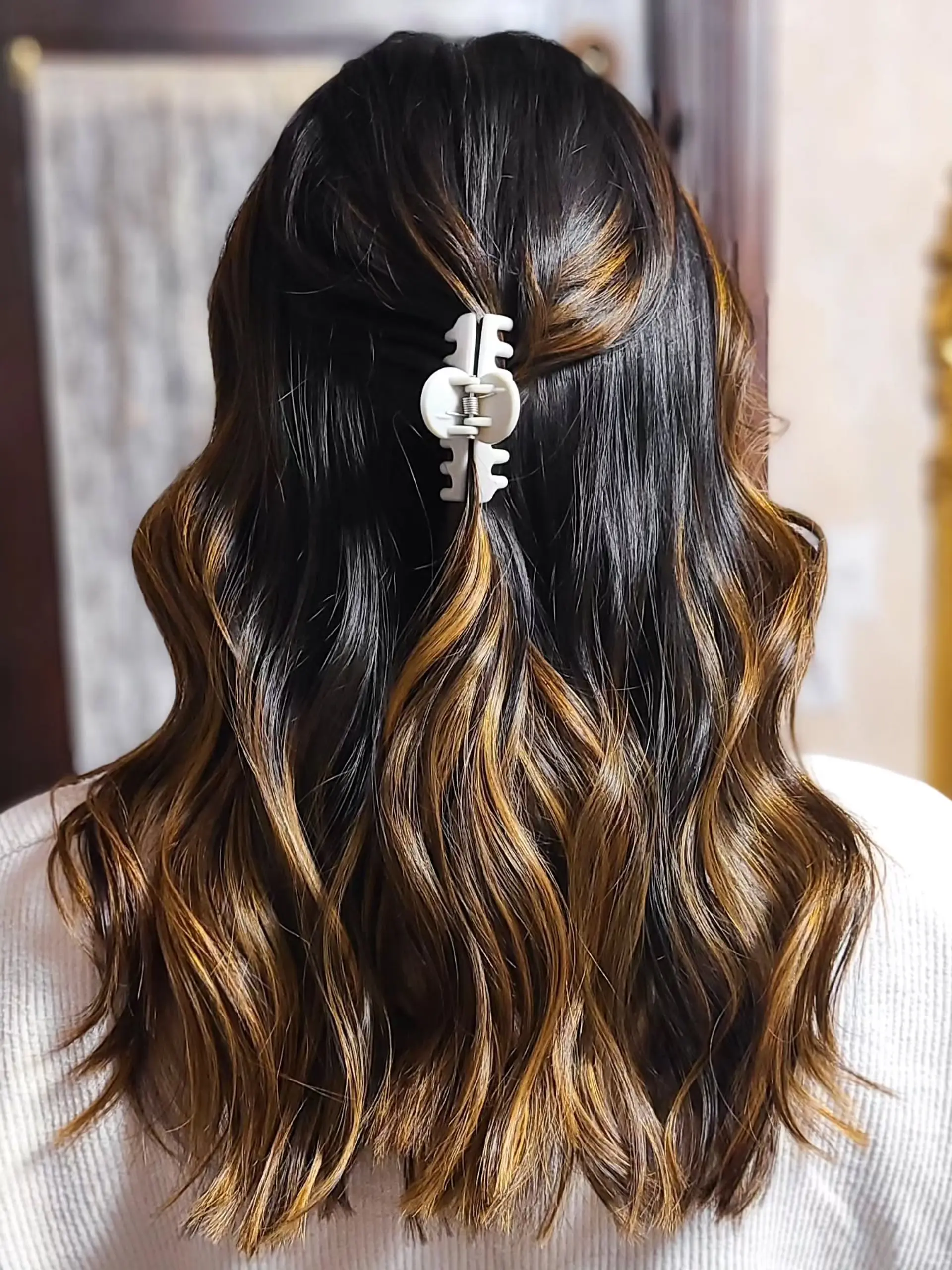 Medium-length wavy hair featuring a dark brown base with caramel and golden brown balayage highlights, styled with a half-up claw clip for an effortless look. 2