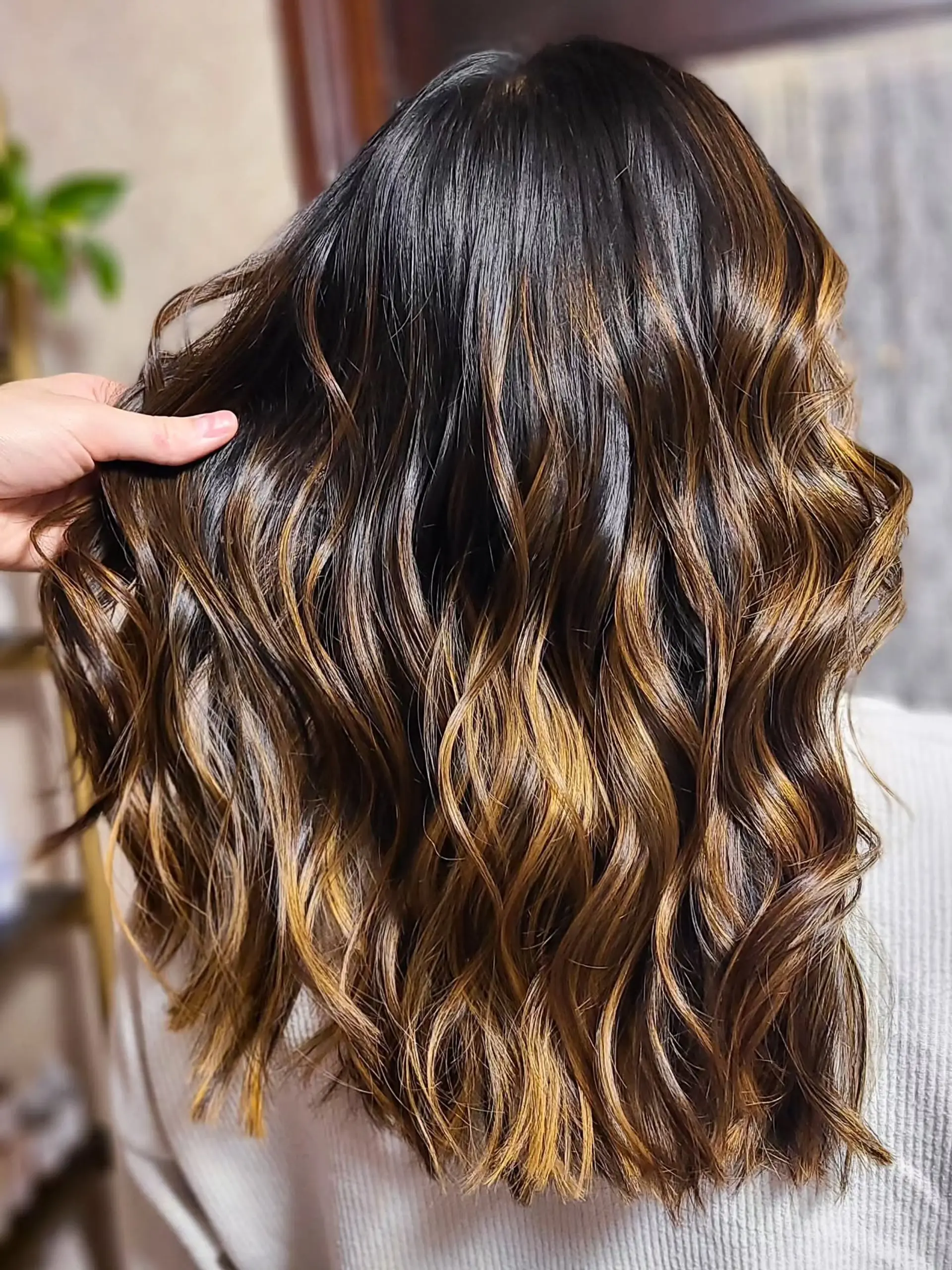 Medium-length wavy hair featuring a dark brown base with caramel and golden brown balayage highlights, styled with a half-up claw clip for an effortless look. 3