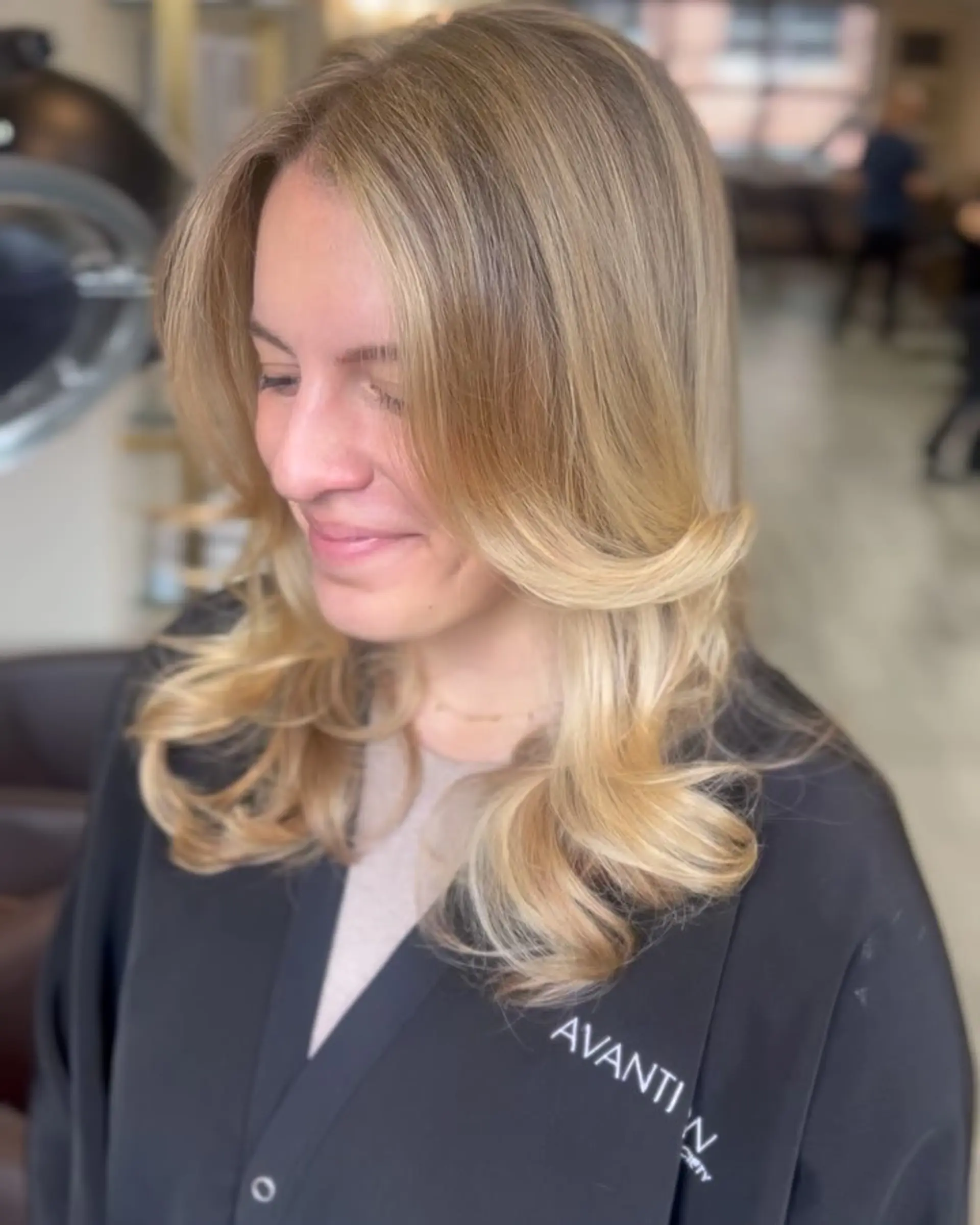 Medium-length golden blonde hair styled in a smooth, voluminous blowout with flipped-out curtain layers and soft curled ends. 1