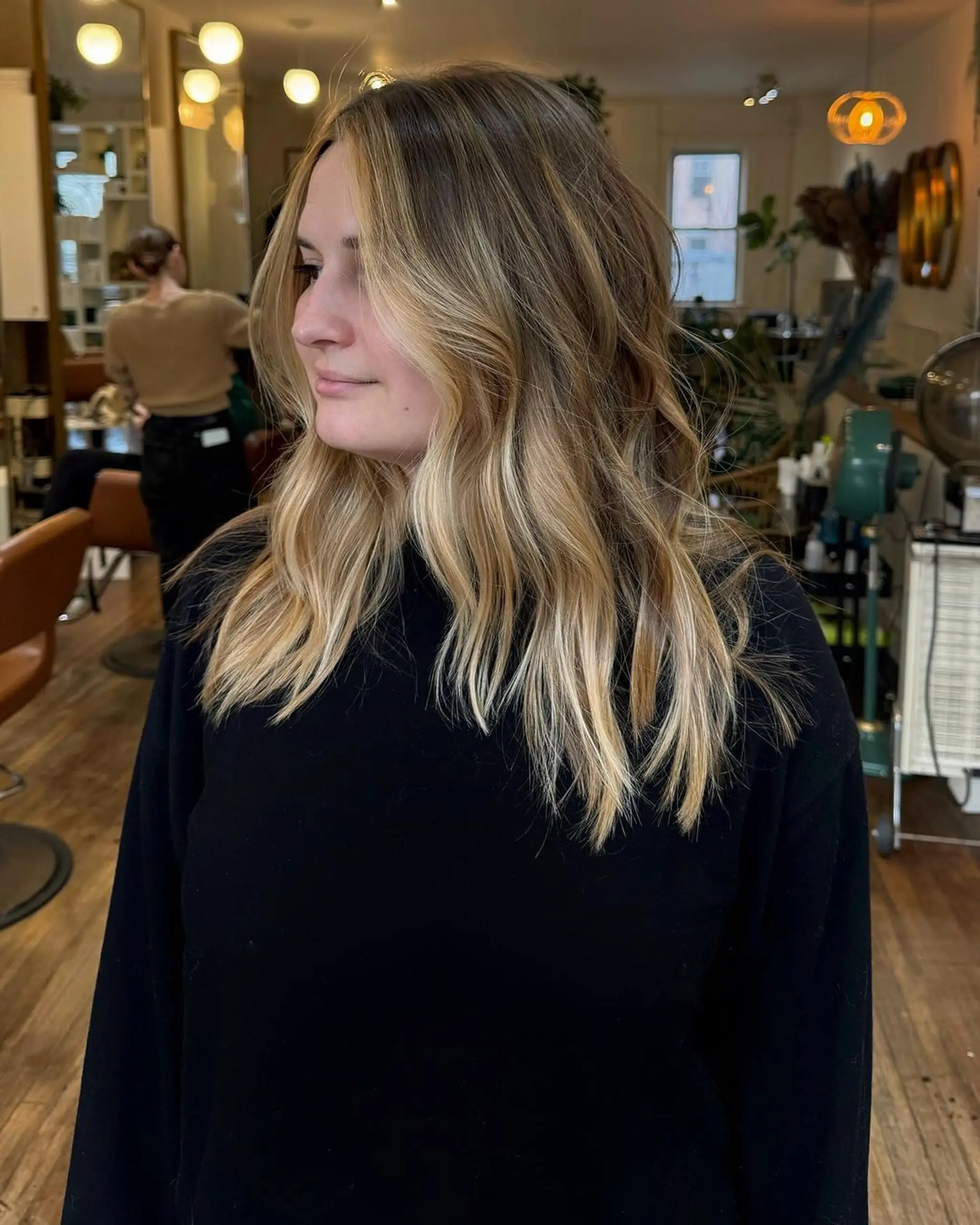 Long, wavy hair with dark blonde roots softly blending into honey blonde balayage, complete with loose waves and face-framing layers.