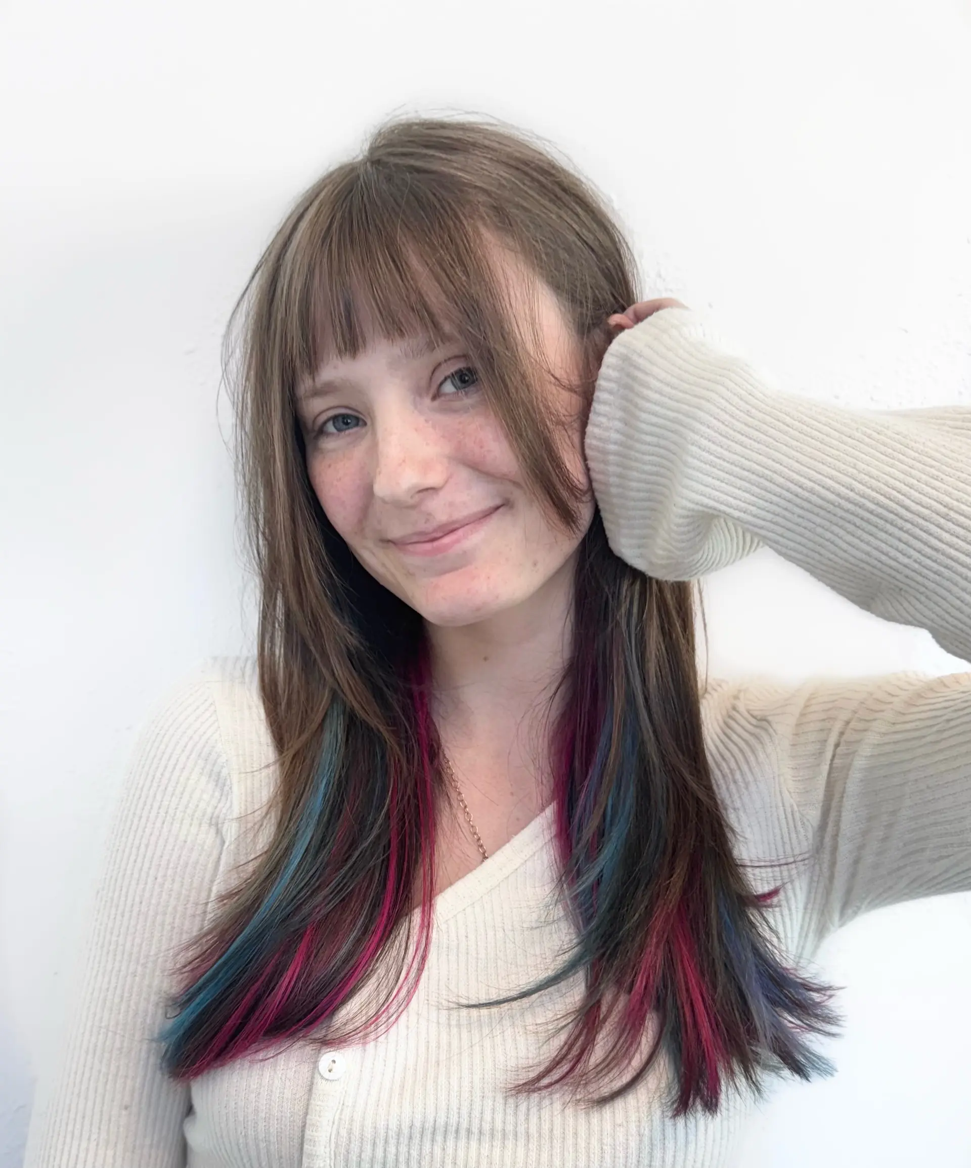 Long straight brunette hair with full straight-across bangs featuring vibrant peekaboo slices of magenta pink and bright blue hidden beneath the top layers. 1