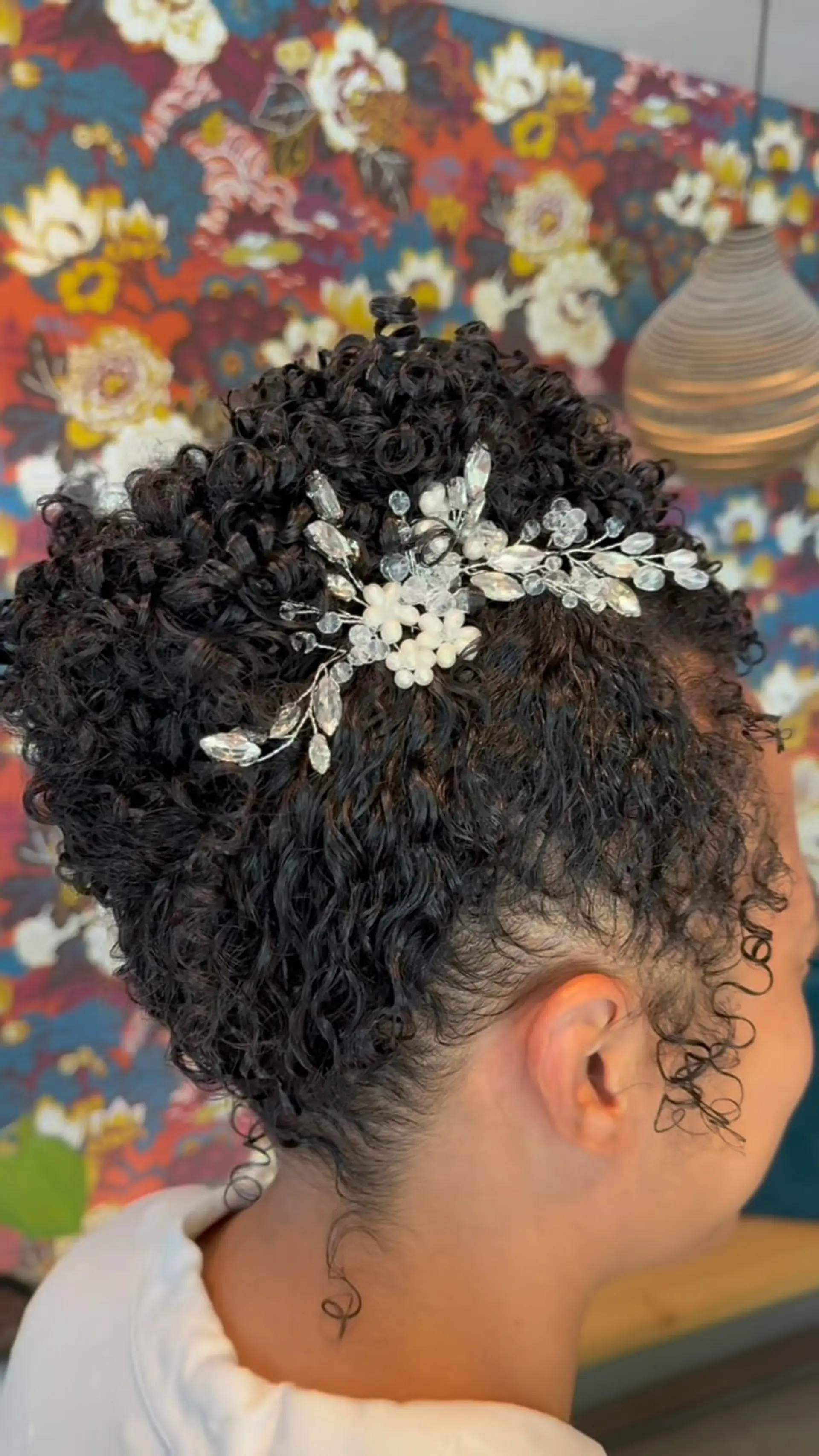 A defined curly bridal updo styled with a sparkling crystal and pearl floral hairpiece tucked into the curls. 1