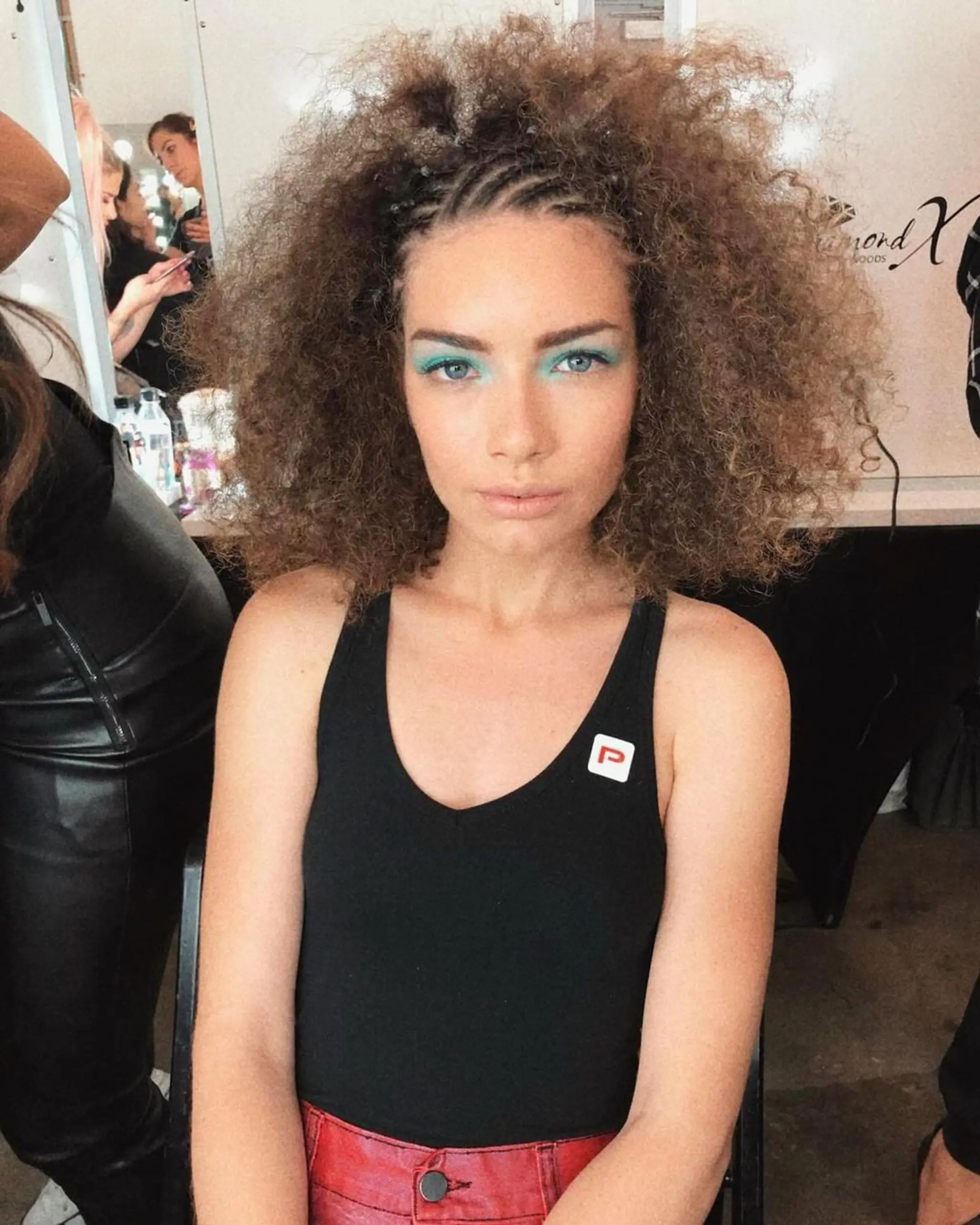 A unique braided halo with frontal cornrows blending into voluminous, dark blonde curls, emphasizing both structure and volume.
