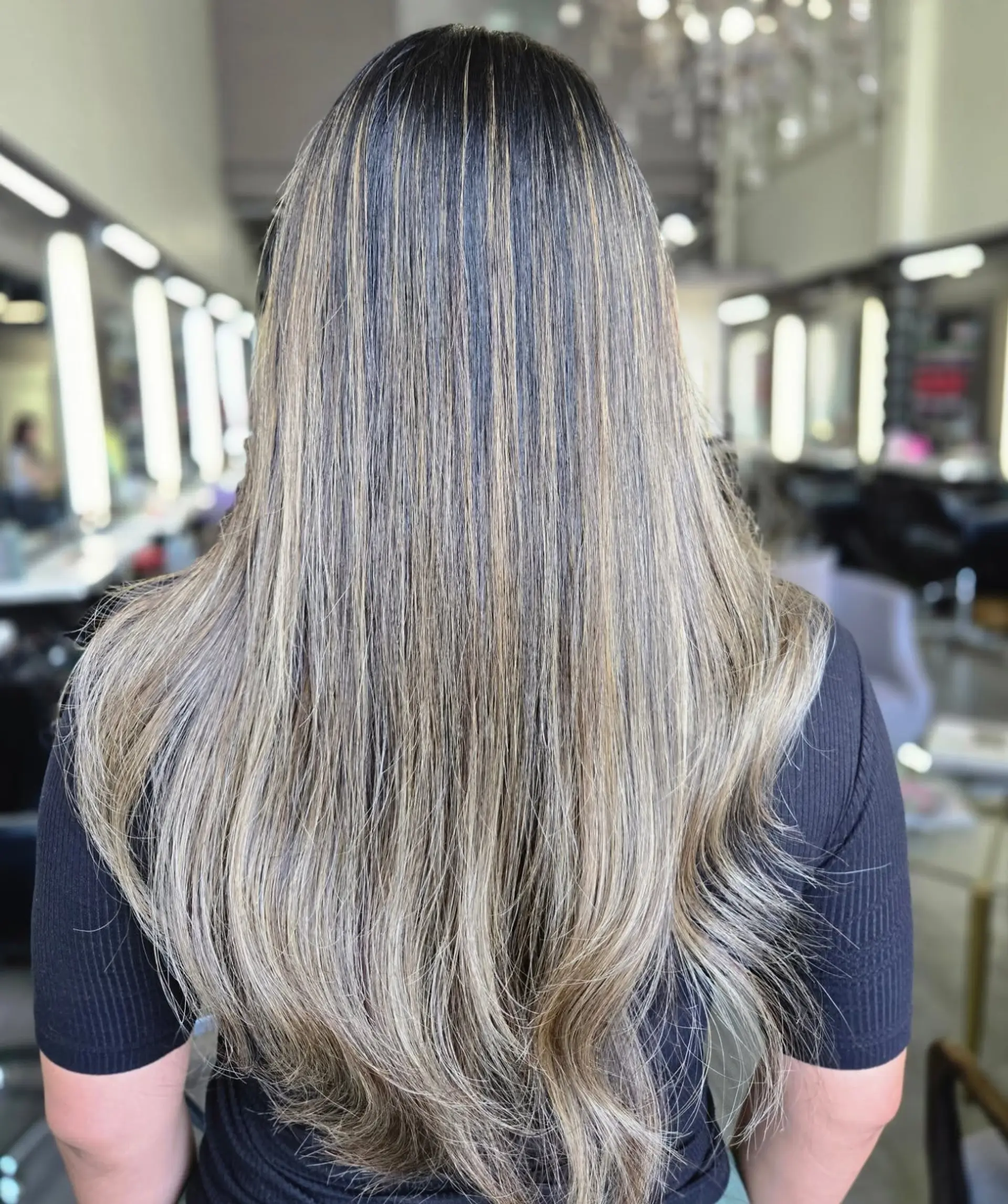 Long dark brown hair styled straight with gentle movement at the ends, featuring finely blended blonde highlights throughout. 1