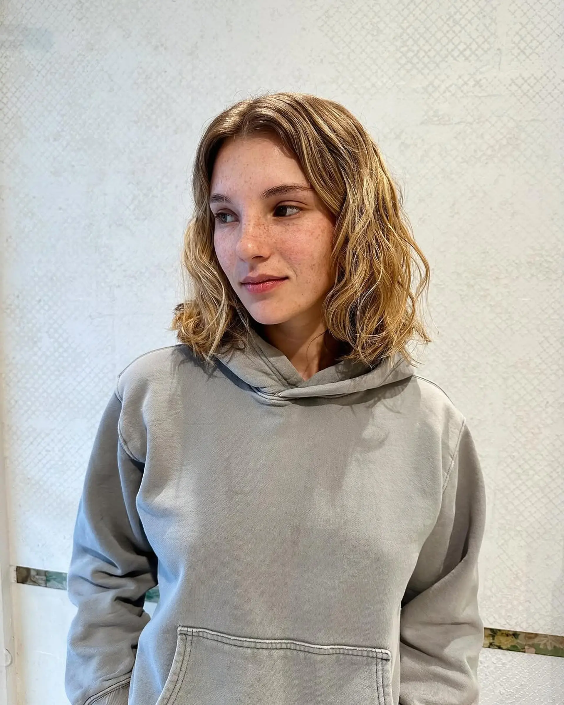 Wavy, medium-length hair with a blend of blonde and light brown hues. Features natural waves with face-framing layers and warm tones. 1