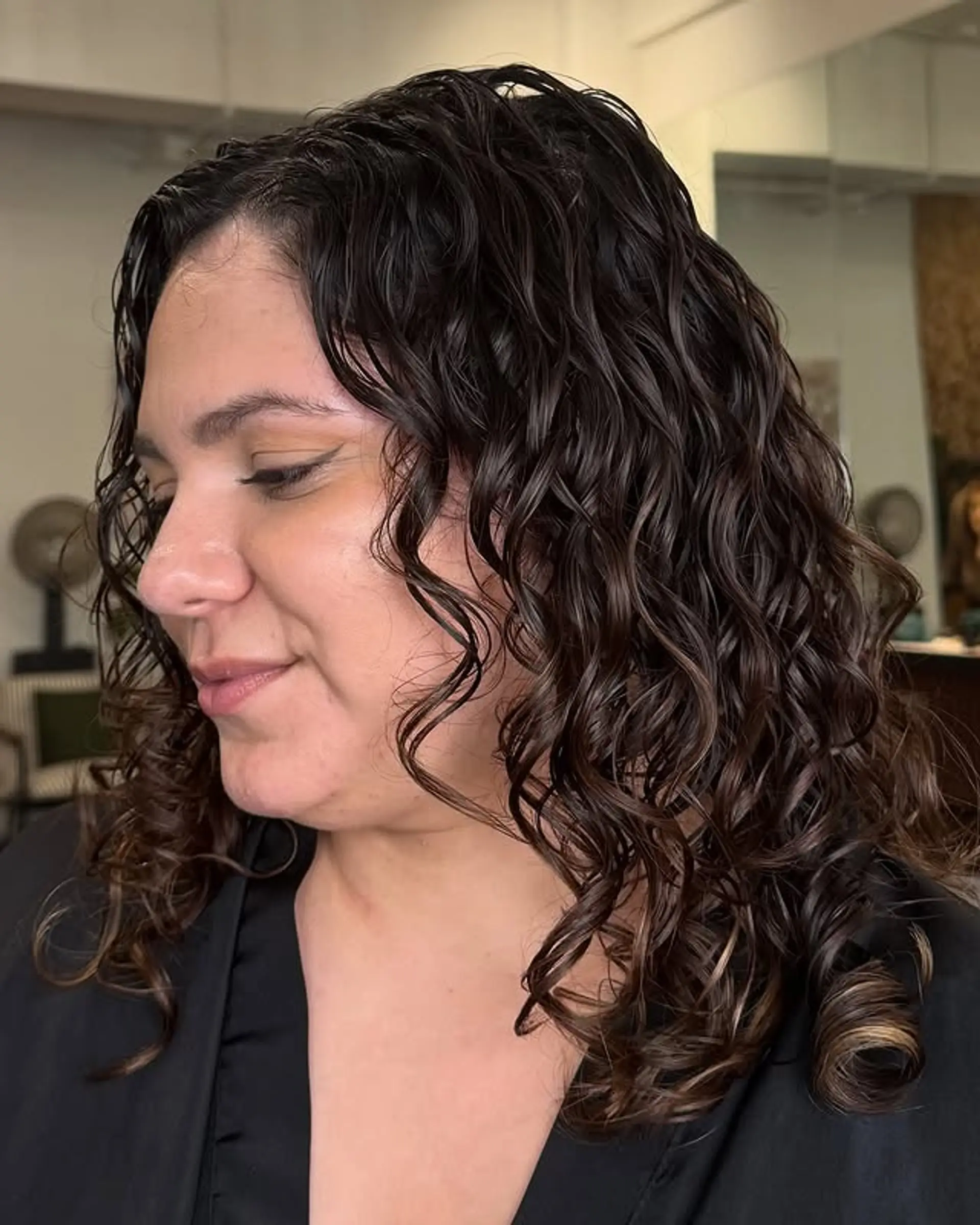 This medium-length curly hairstyle features natural brown hair with bronzed highlights, creating a warm and dimensional look. 1