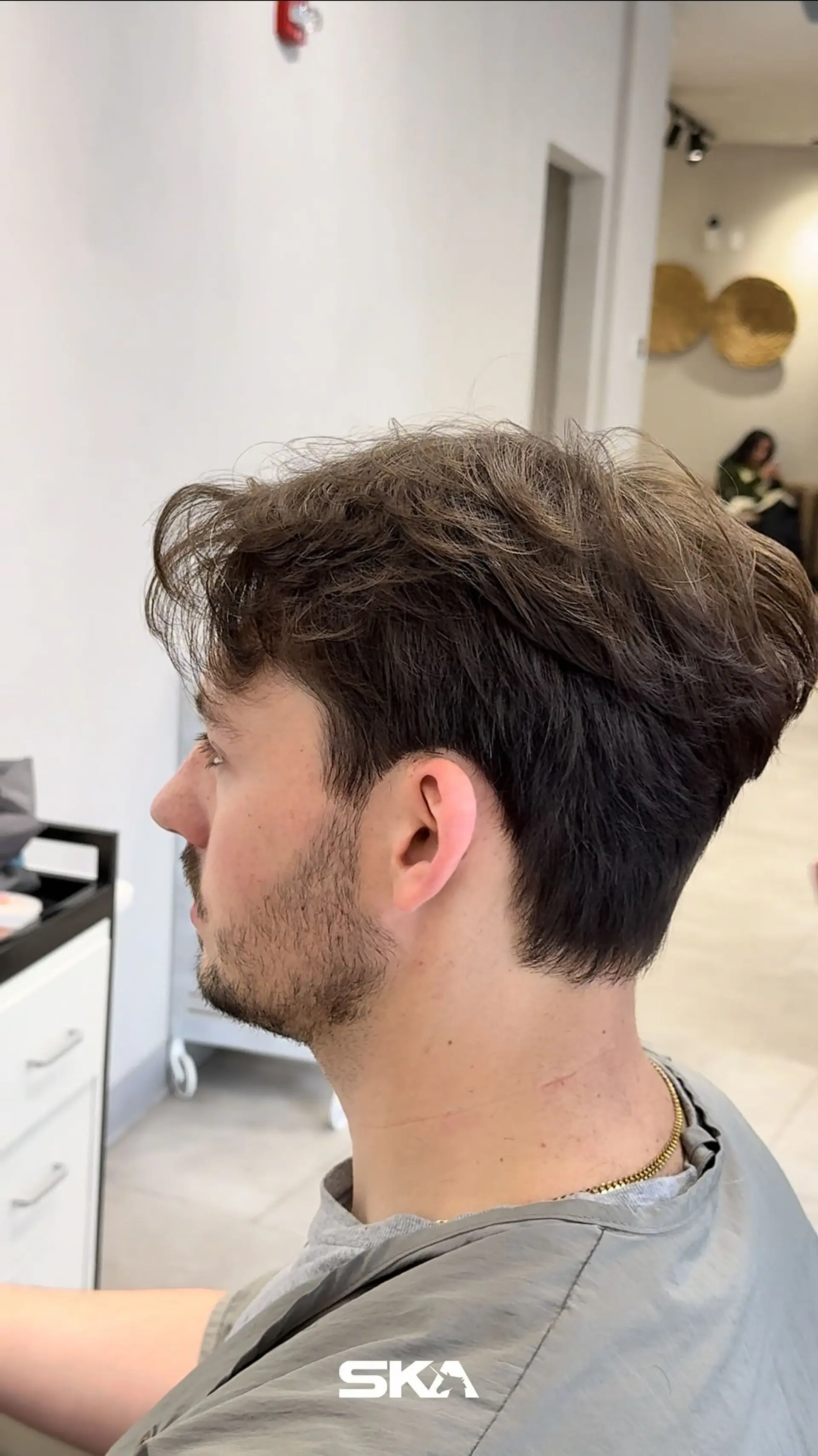 A men's textured haircut featuring softly tapered sides and neckline with a fuller, piecey top that naturally falls forward. 1