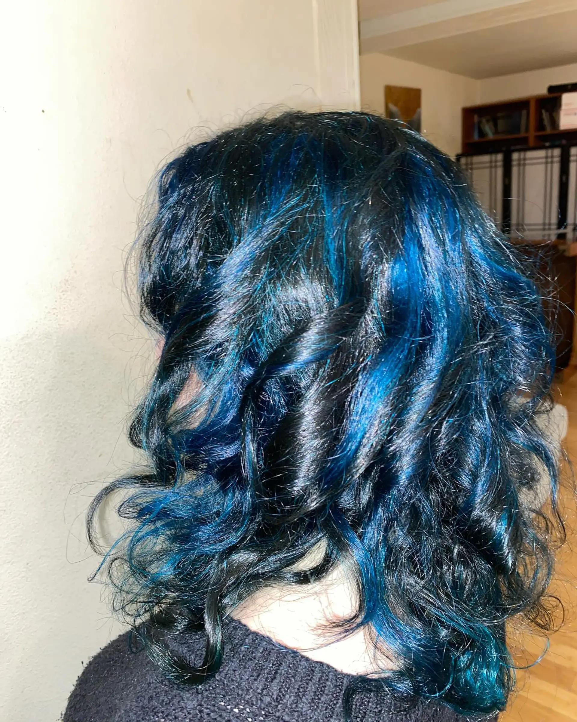 Medium-length wavy black hair with striking, vibrant chunky blue highlights styled in loose curls. 1