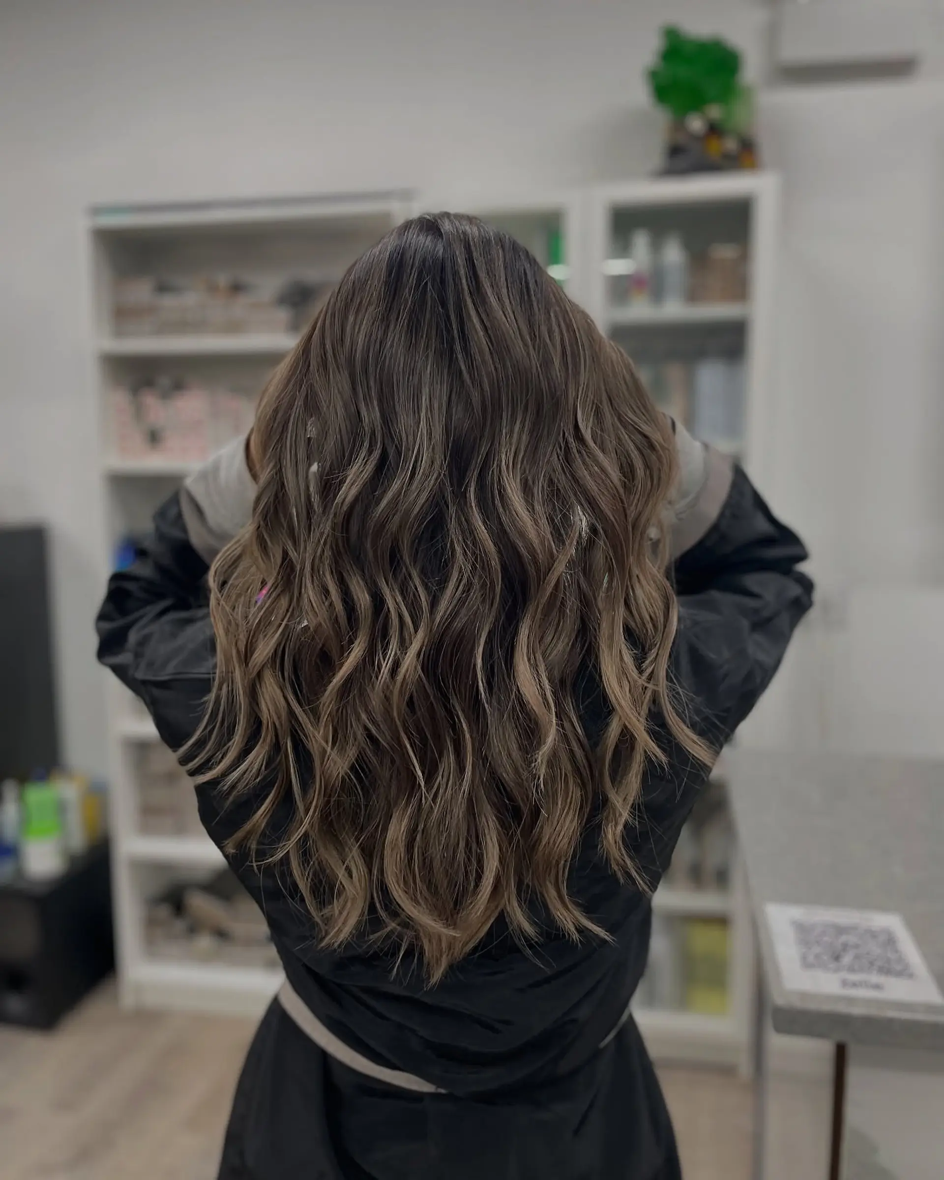 Long, wavy brunette hair with blonde balayage highlights. The hair is layered to enhance the wave pattern. 1