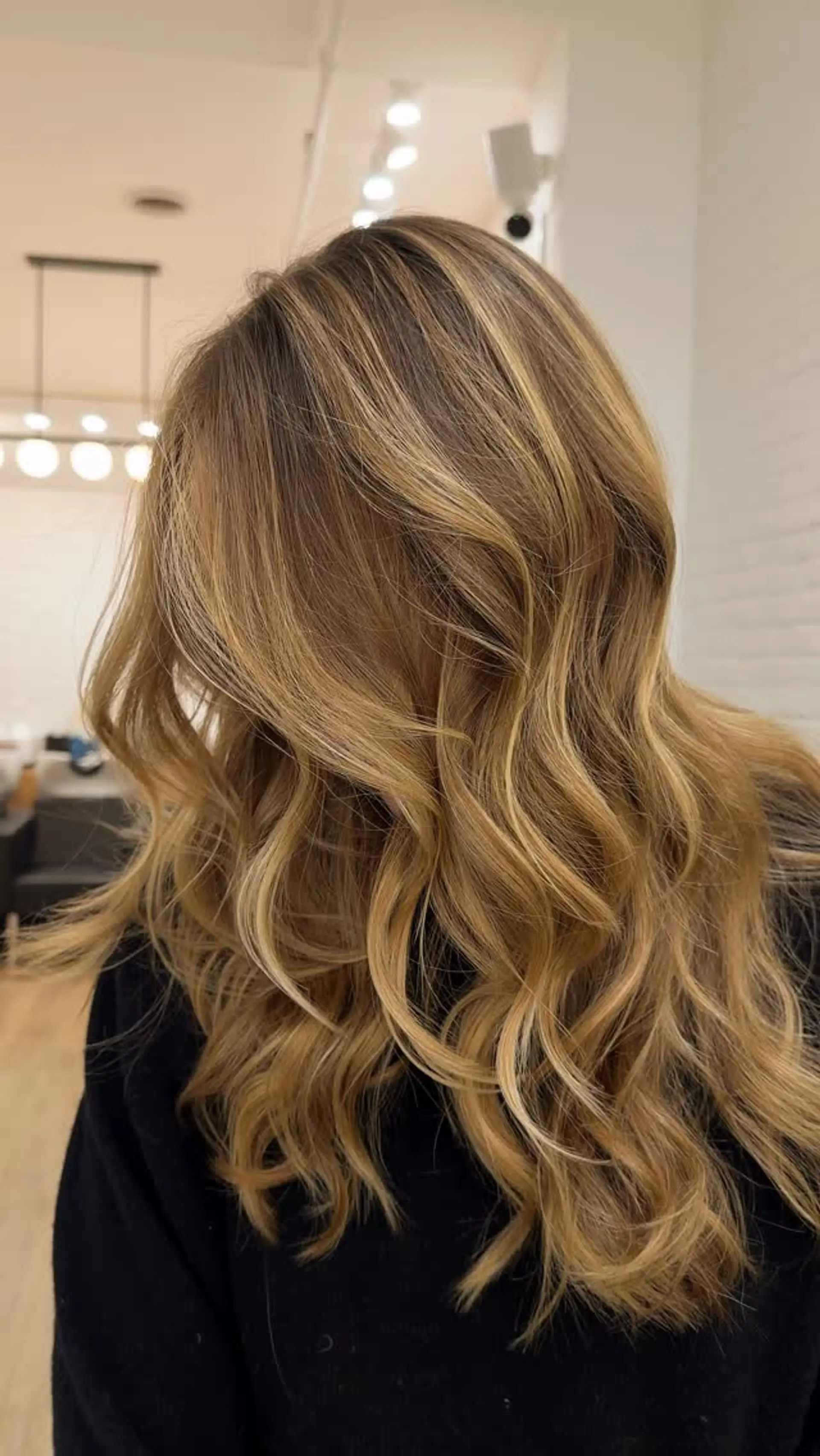 Long honey blonde hair featuring seamless dimensional balayage highlights styled in soft, bouncy waves. 1