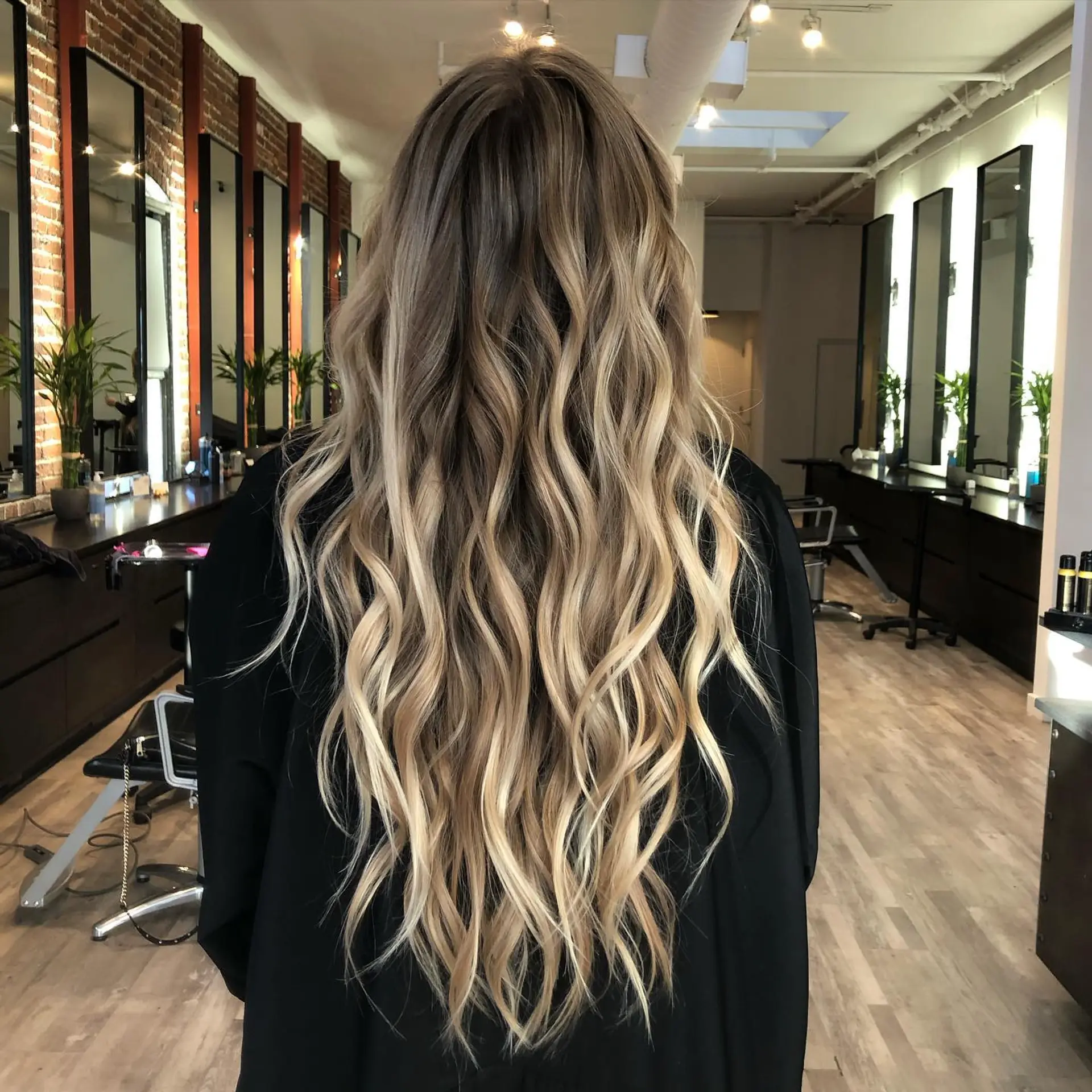 Very long, flowing hair styled in loose beach waves featuring a seamless blonde balayage and babylights over a light brown base. 1