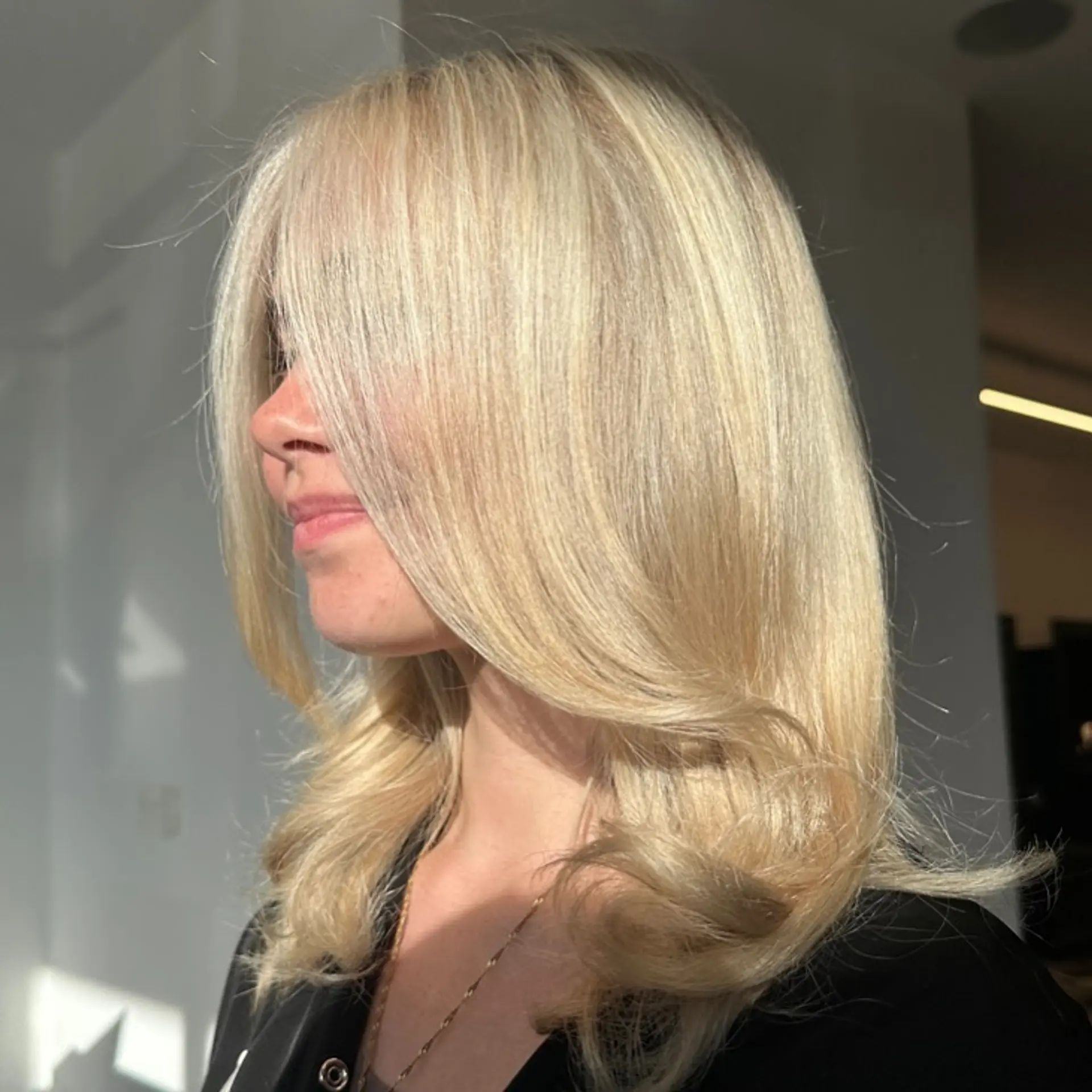 Medium-length bright blonde hair styled in a smooth blowout with long face-framing fringe and flipped ends. 1