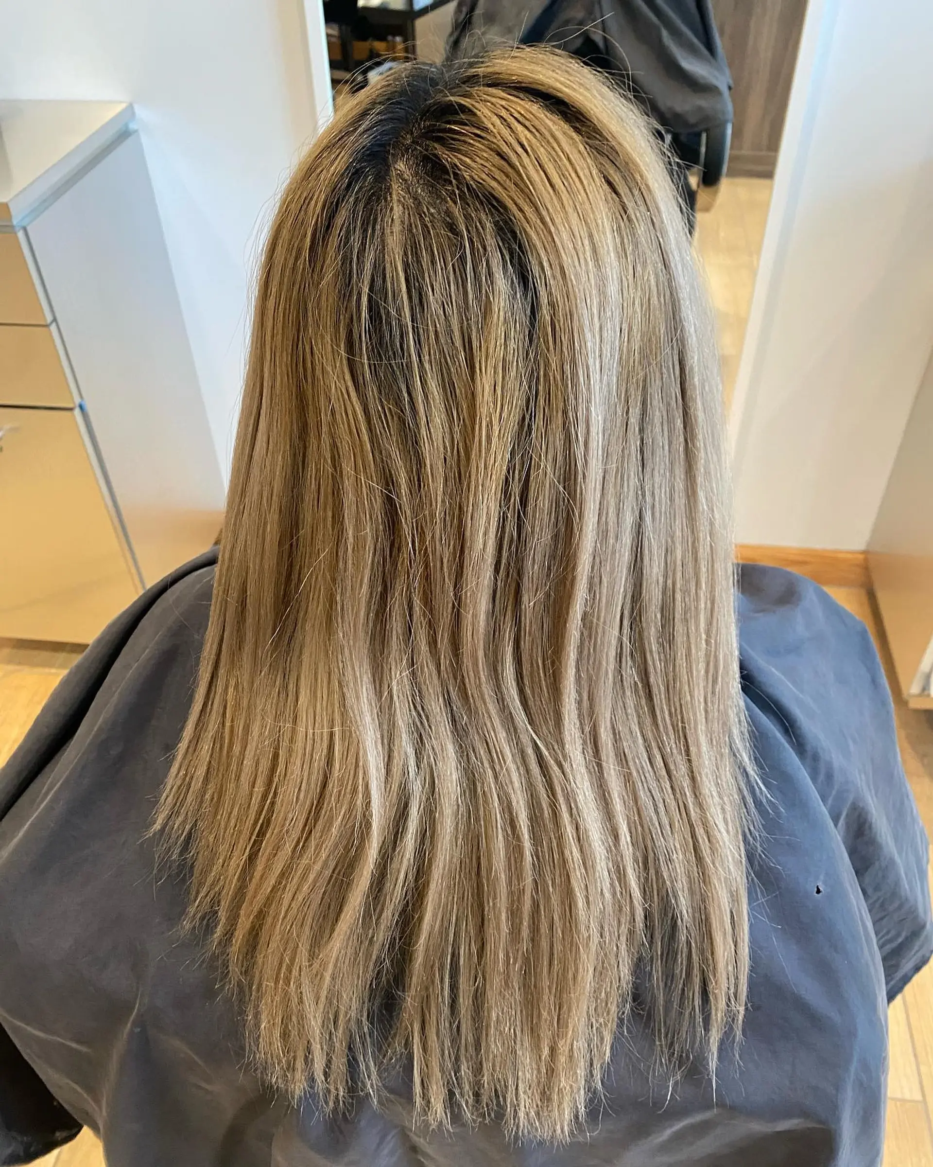 Long, straight bleached blonde hair worn down smoothly over a salon cape. 1