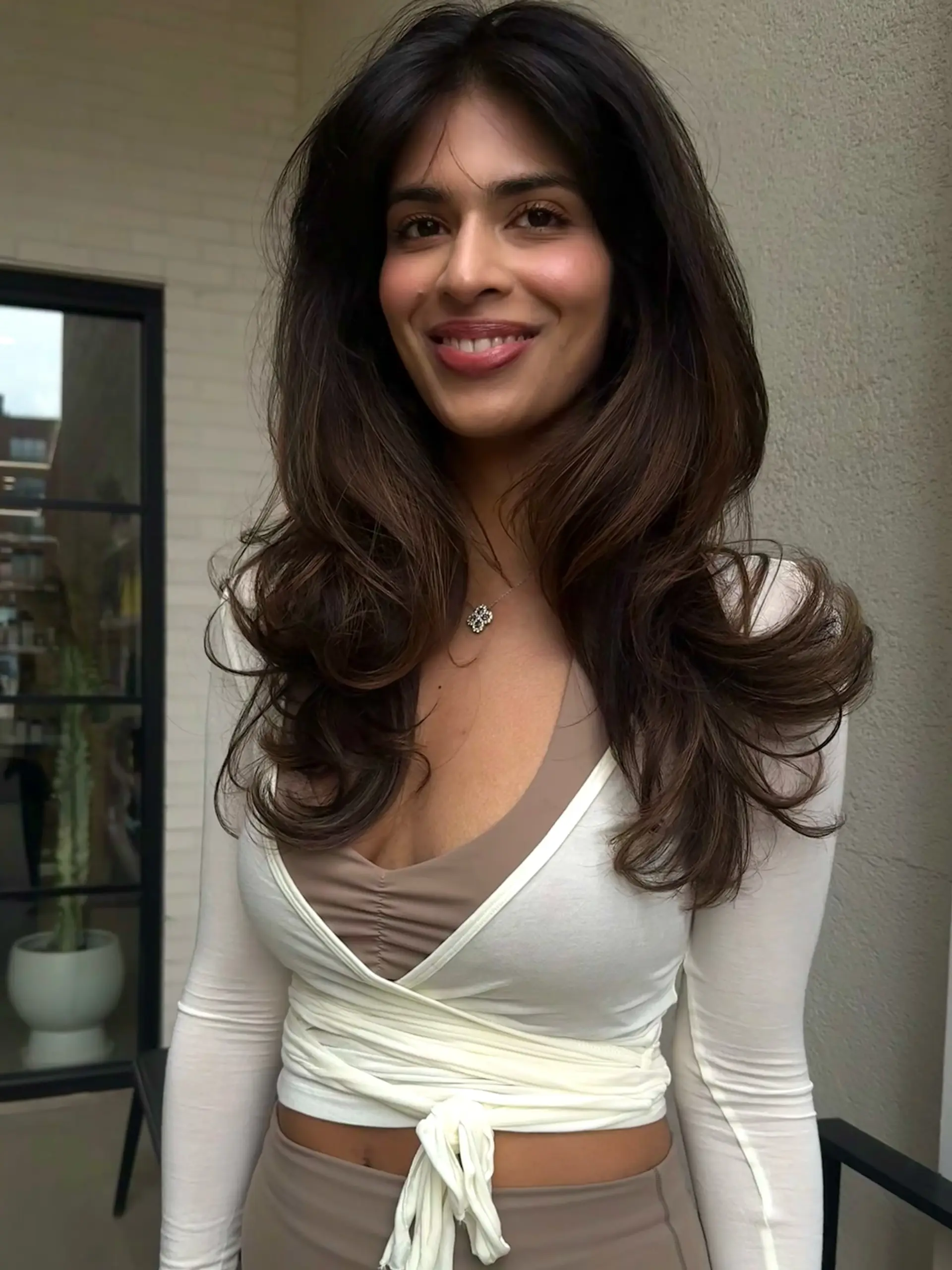 Long dark brunette hair styled into a voluminous, bouncy blowout with flipped ends and subtle face-framing layers. 1