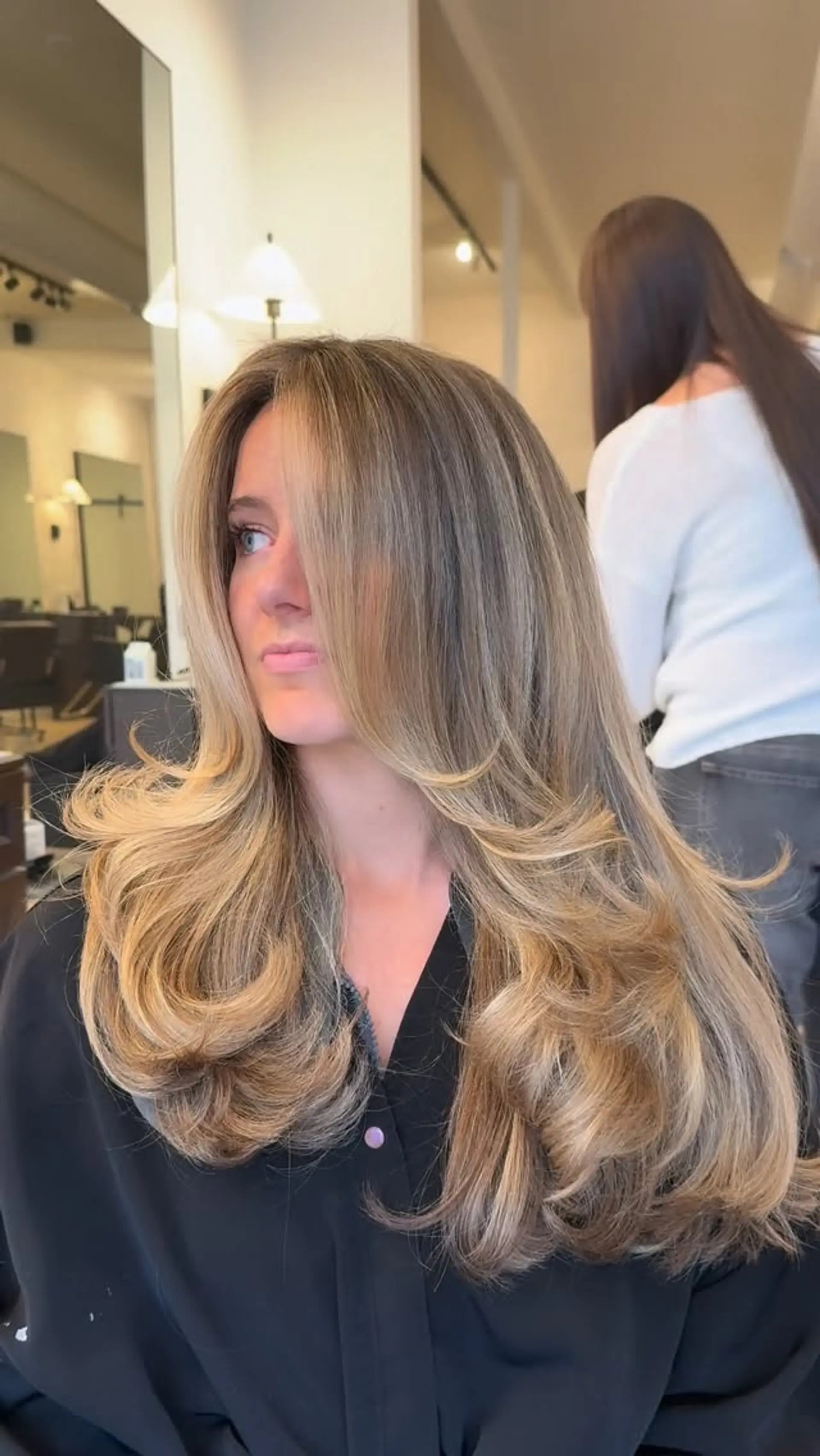 Long layered cut styled with a voluminous roller blowout, featuring dimensional blonde highlights and face-framing curves. 1