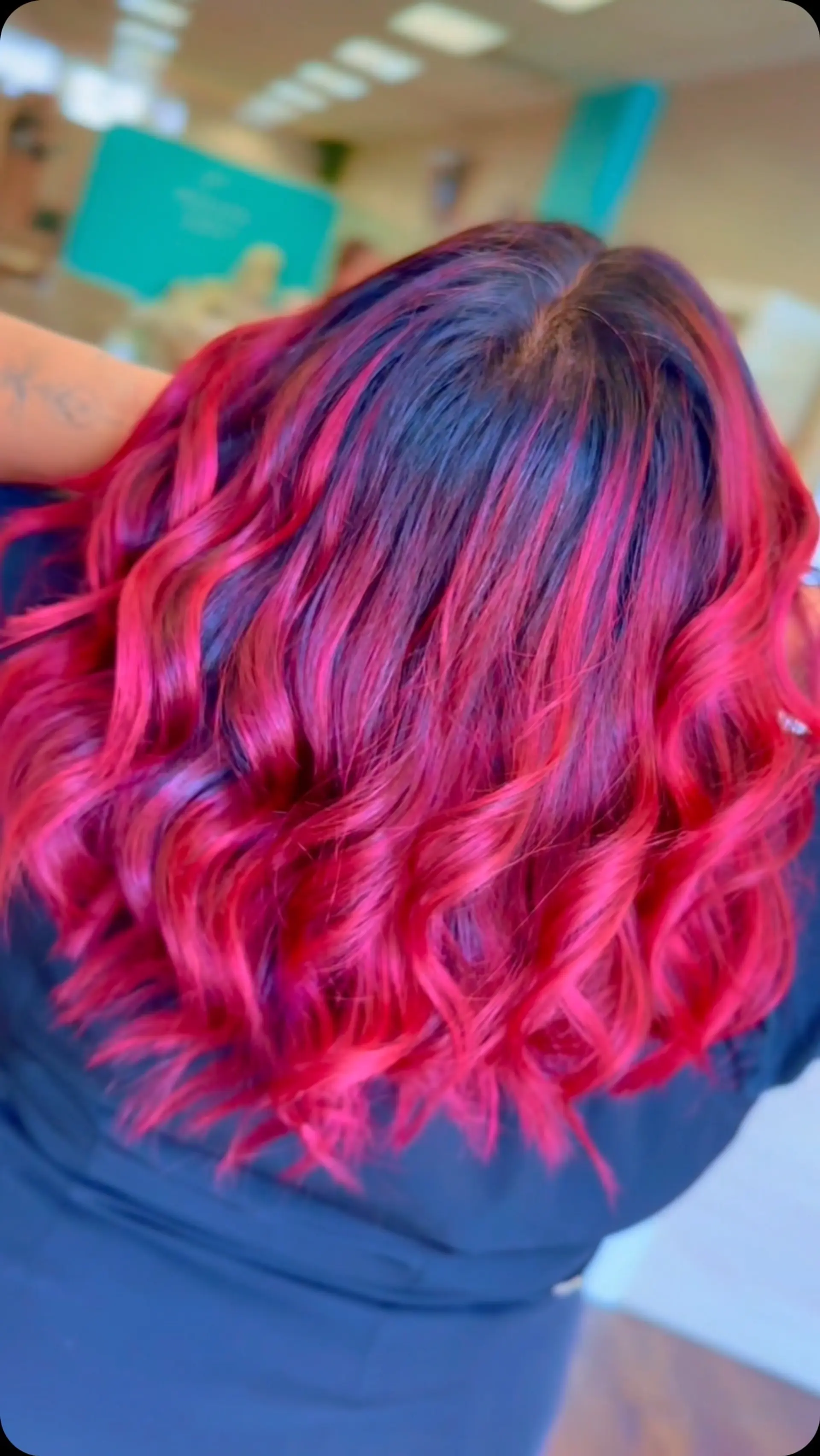 Medium-length layered hair featuring a fiery magenta and crimson red balayage over dark roots, styled in soft wavy iron curls. 1