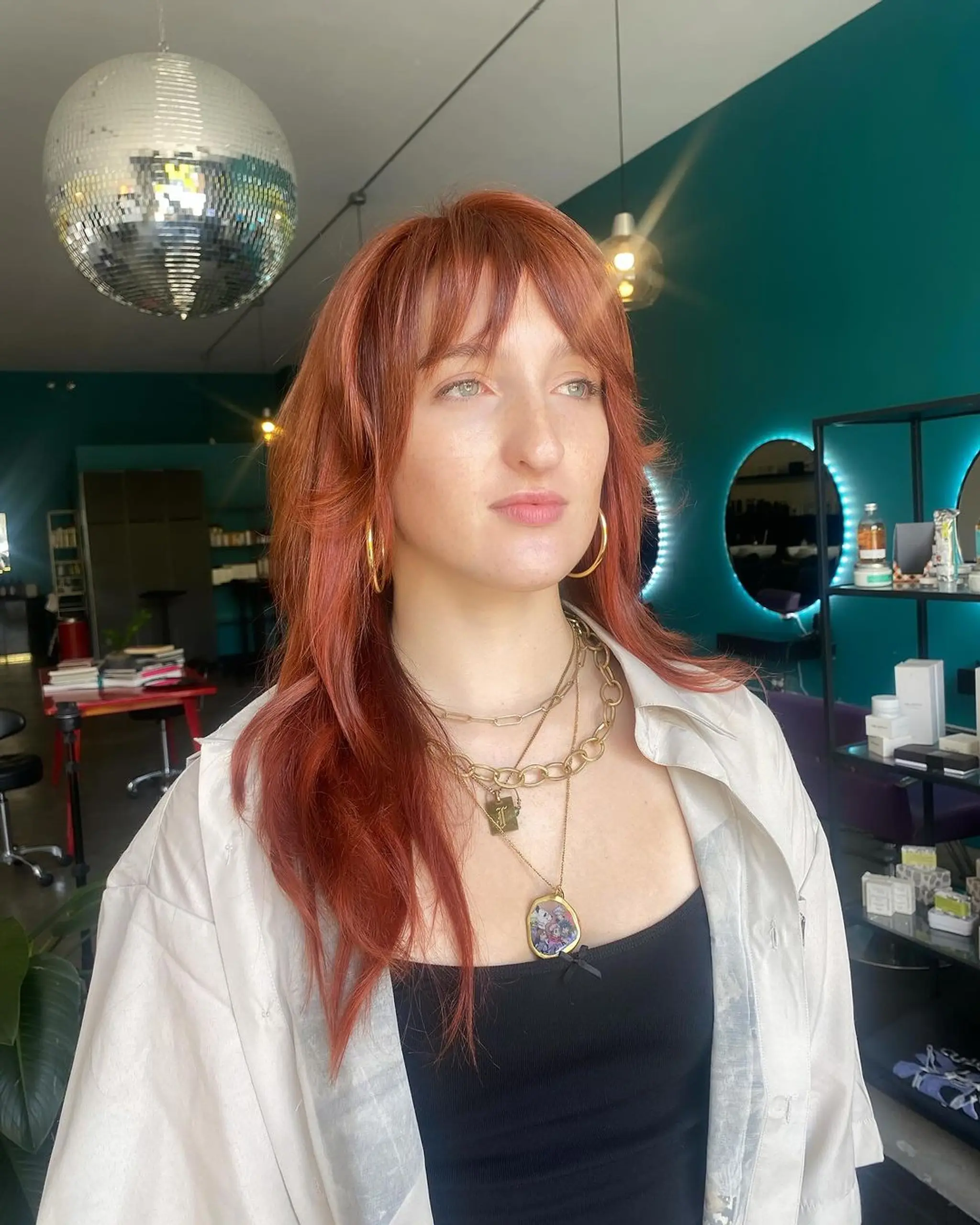 A long, wavy hairstyle in a vibrant copper red, featuring long layers, curtain bangs, and feathered ends for a soft, voluminous look.
